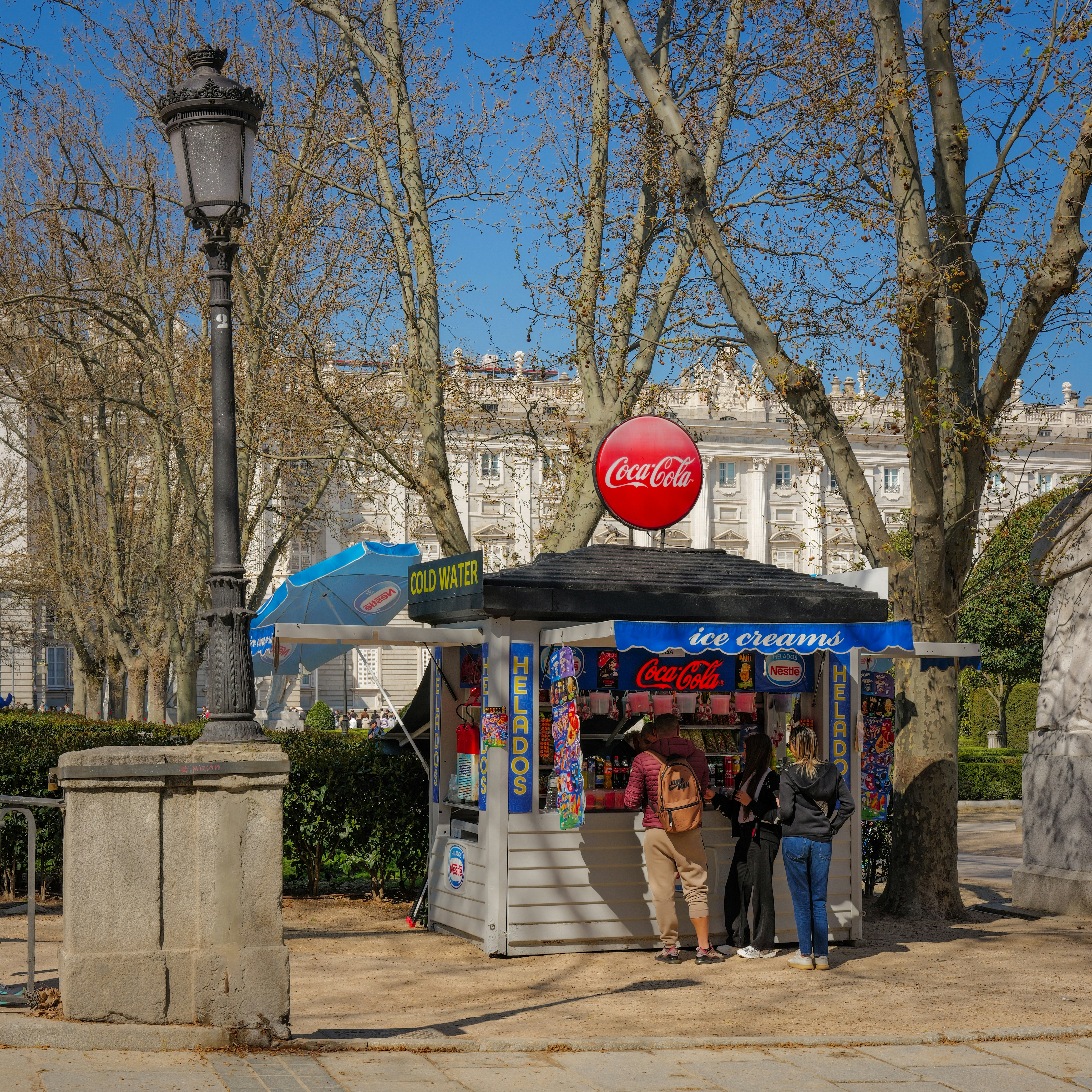 Kiosk with coca-cola sign and people buying items.