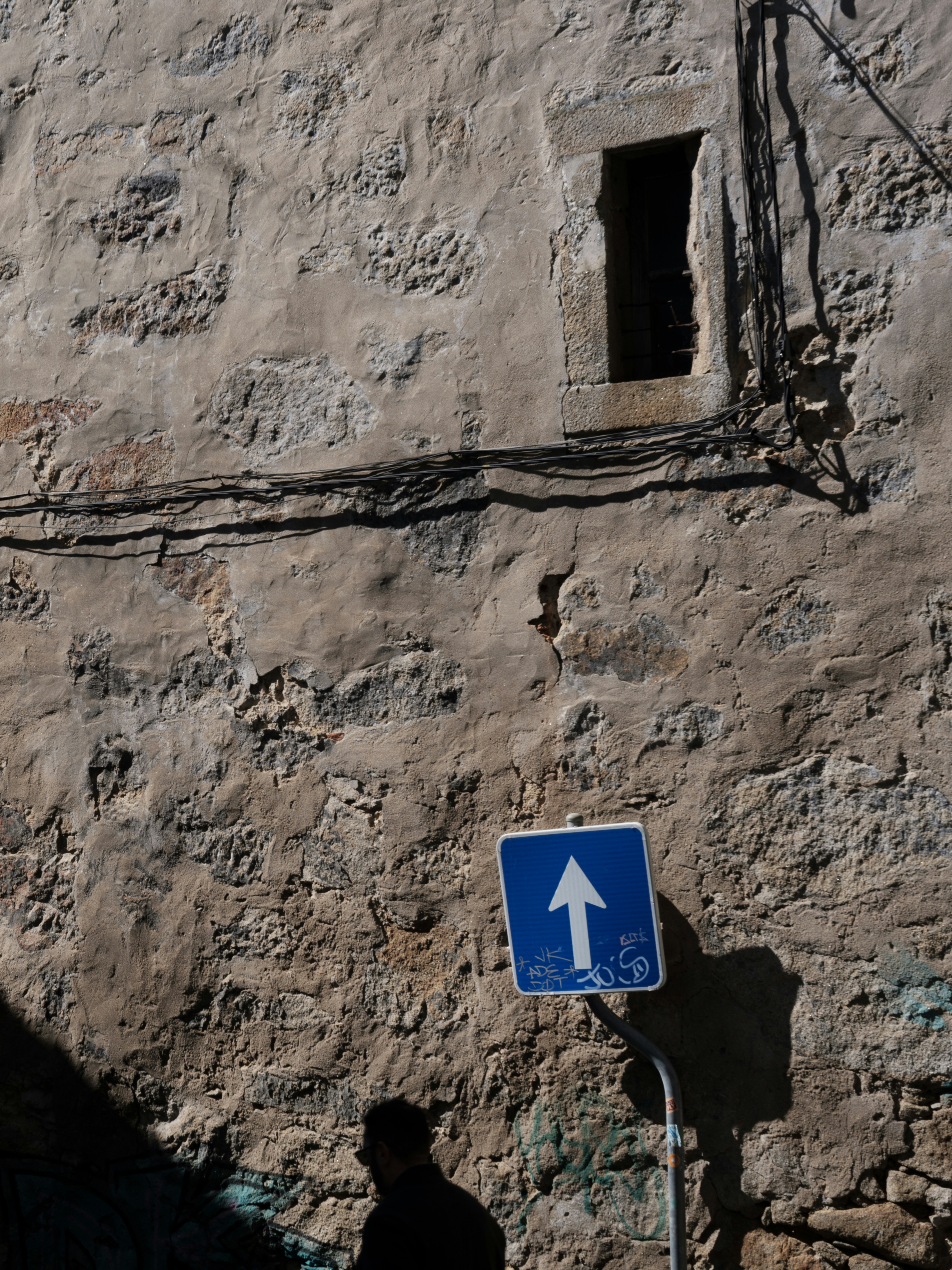 A silhouette of a person walks past a street sign.