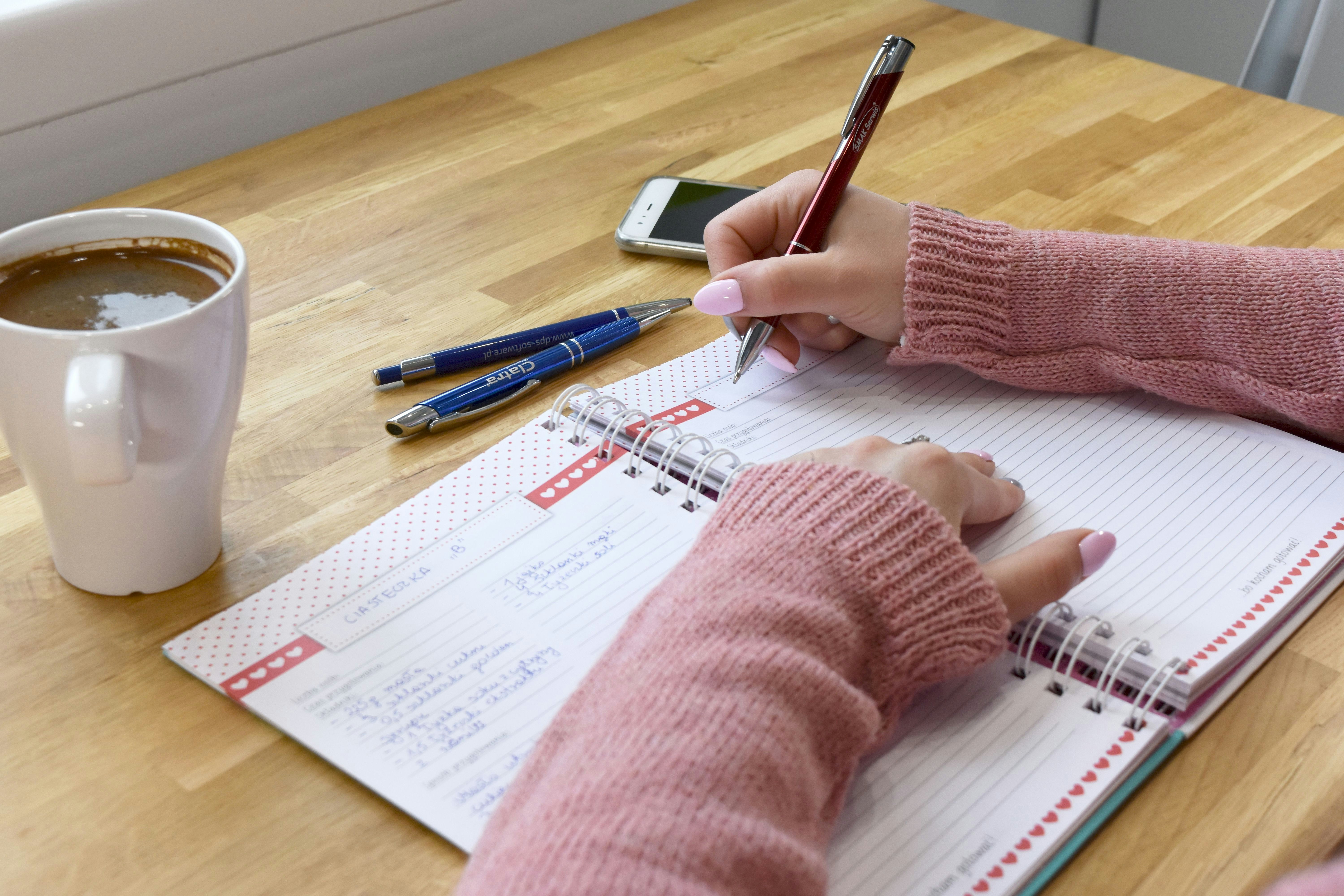 A person writing in a notebook with coffee.