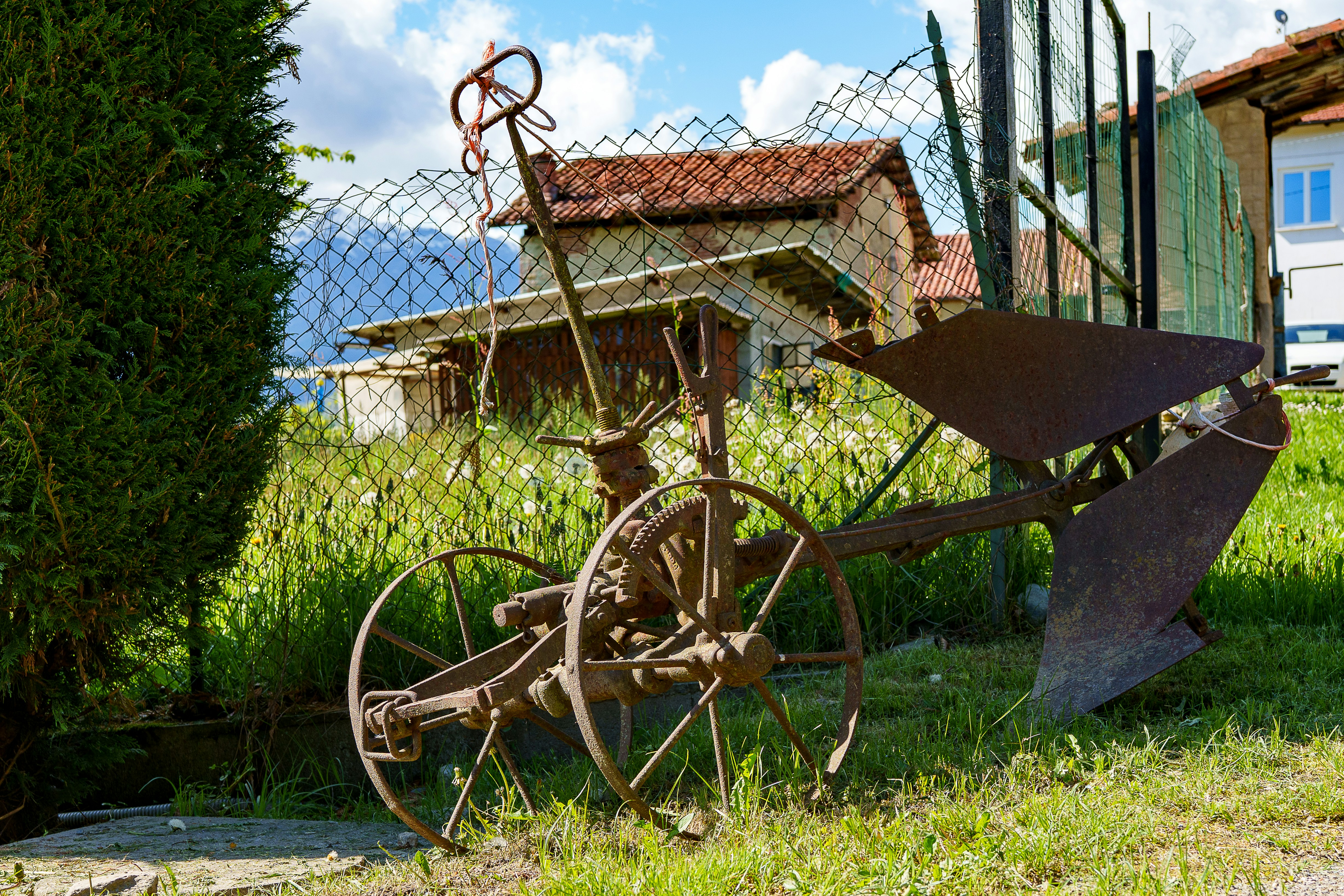 Old rusty plow sits in a grassy yard.