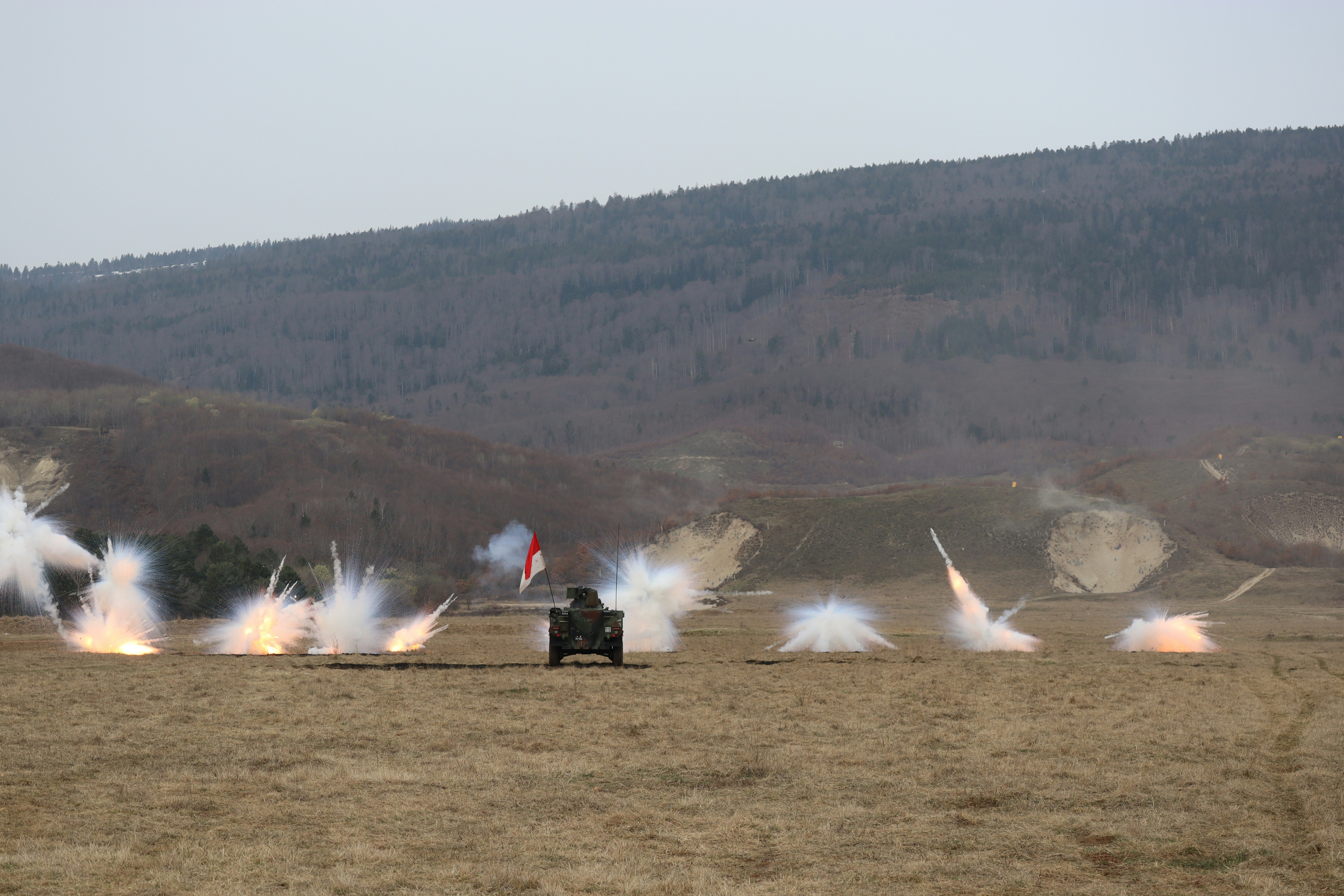 装甲車両が野原で複数発の砲弾を発射します。