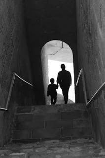 Two figures walk down a stone staircase towards light.