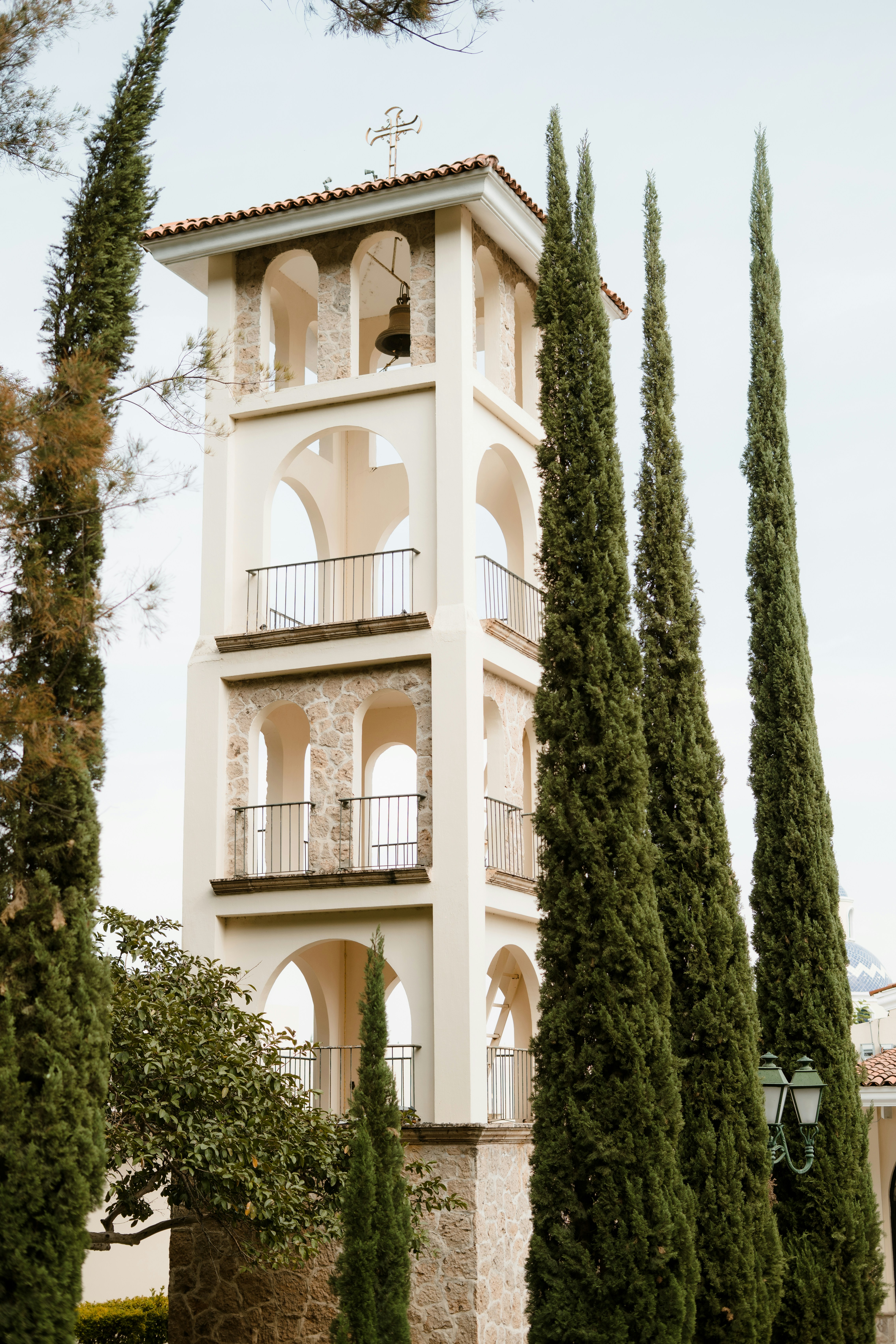 Ein hoher Glockenturm mit gewölbten Öffnungen und Zypressen.