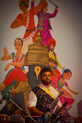 Man in traditional attire with cultural mural behind him