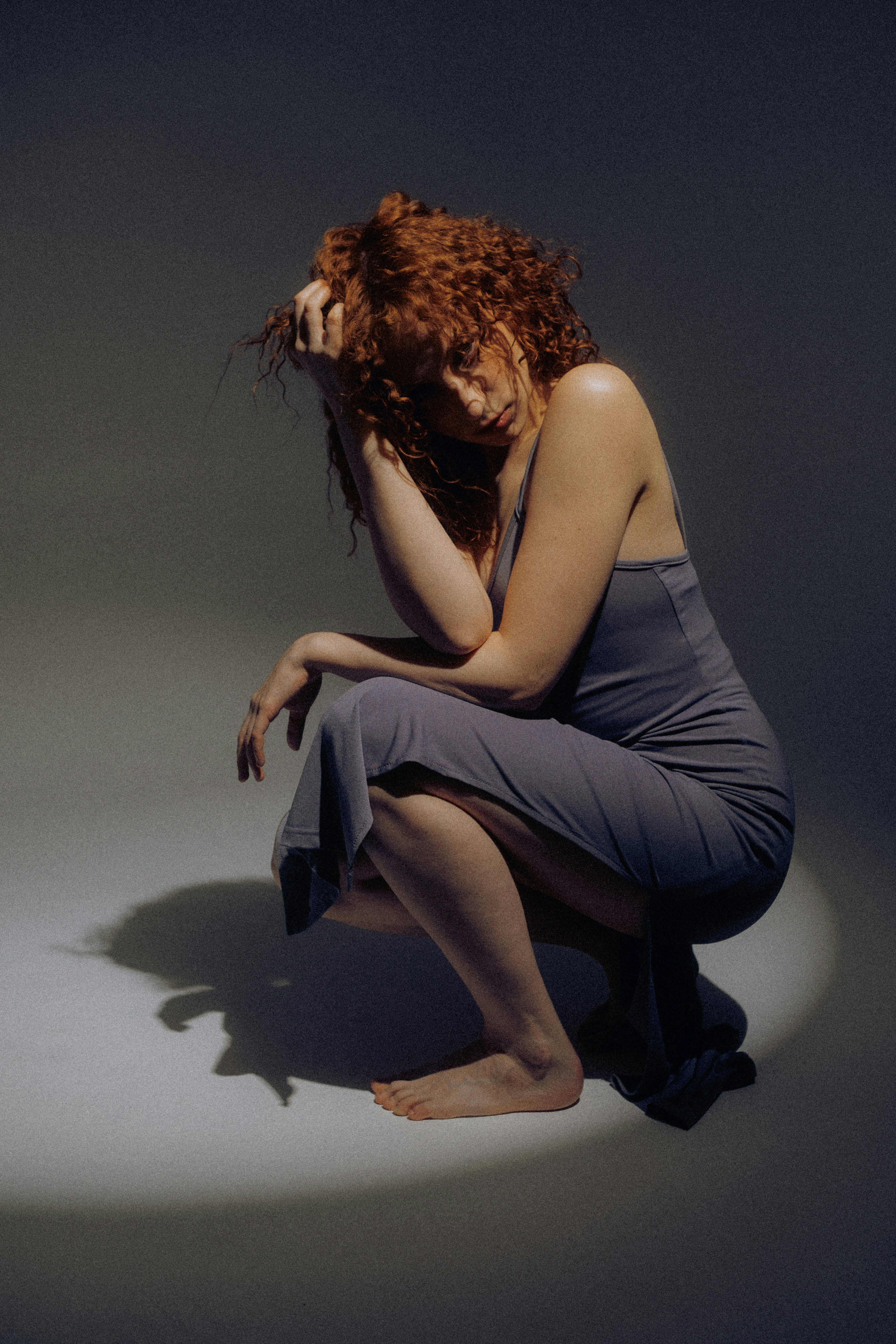 Donna con capelli rossi e ricci accovacciata in un vestito grigio.