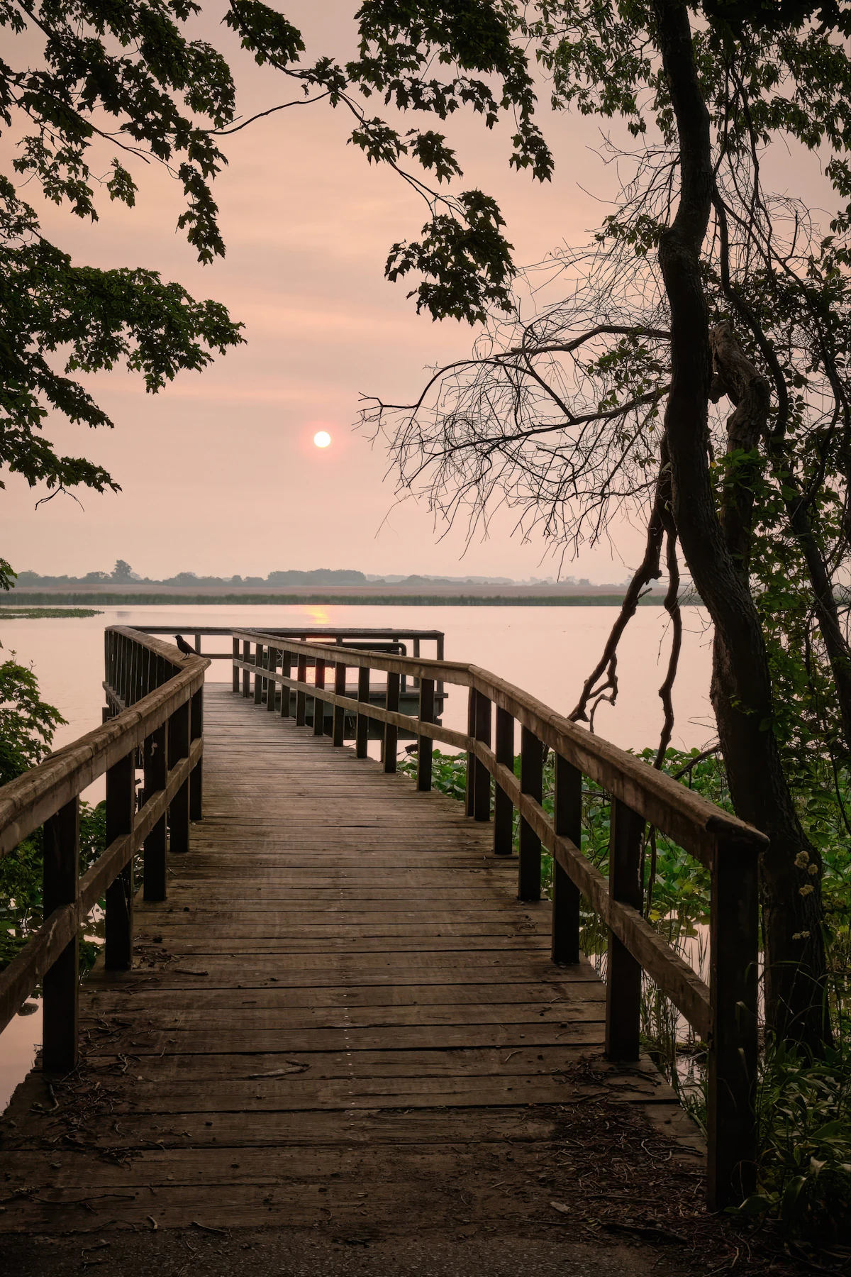 Ponton de bois s'avançant sur un lac au lever du soleil