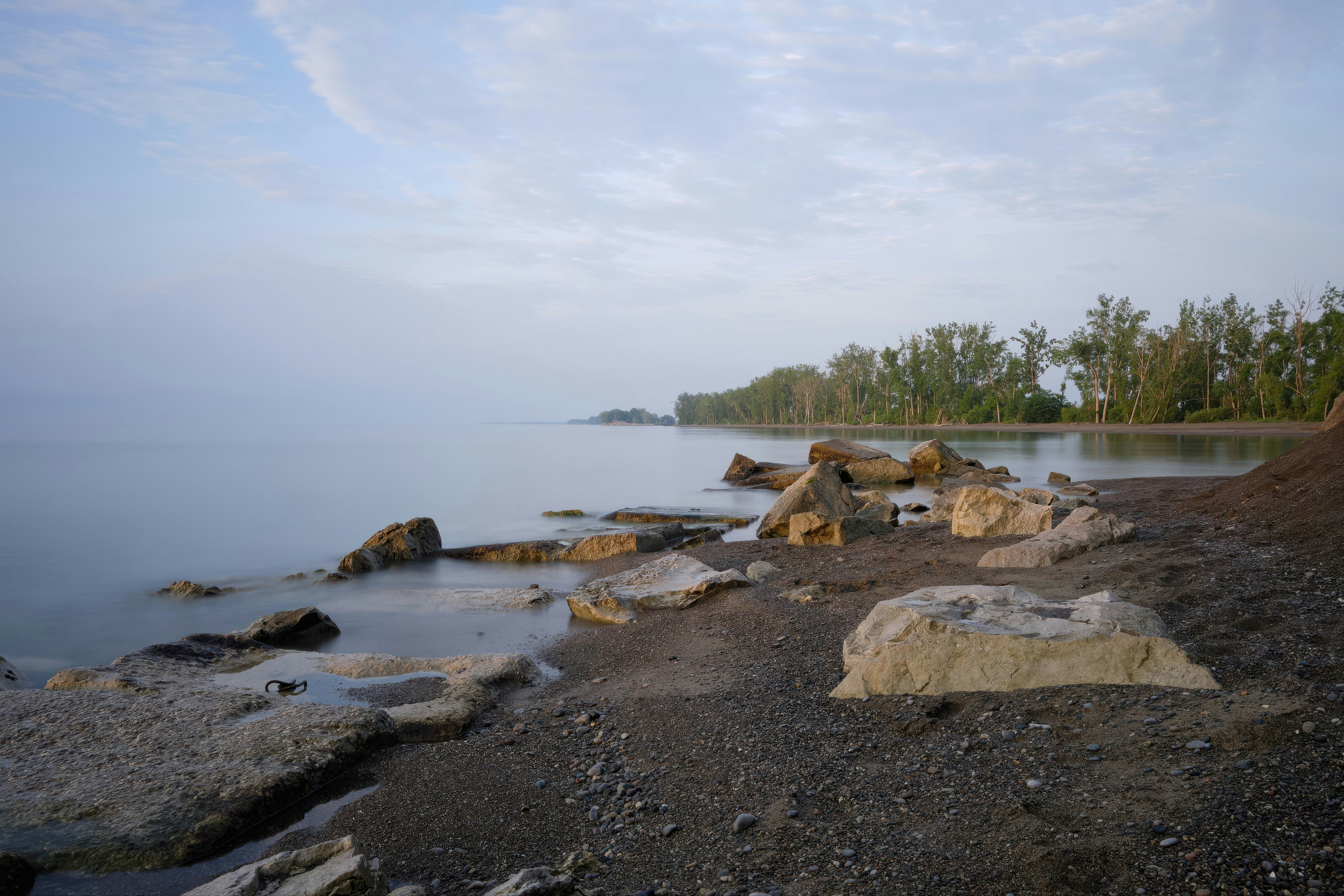 Rocky shoreline with calm water and distant trees