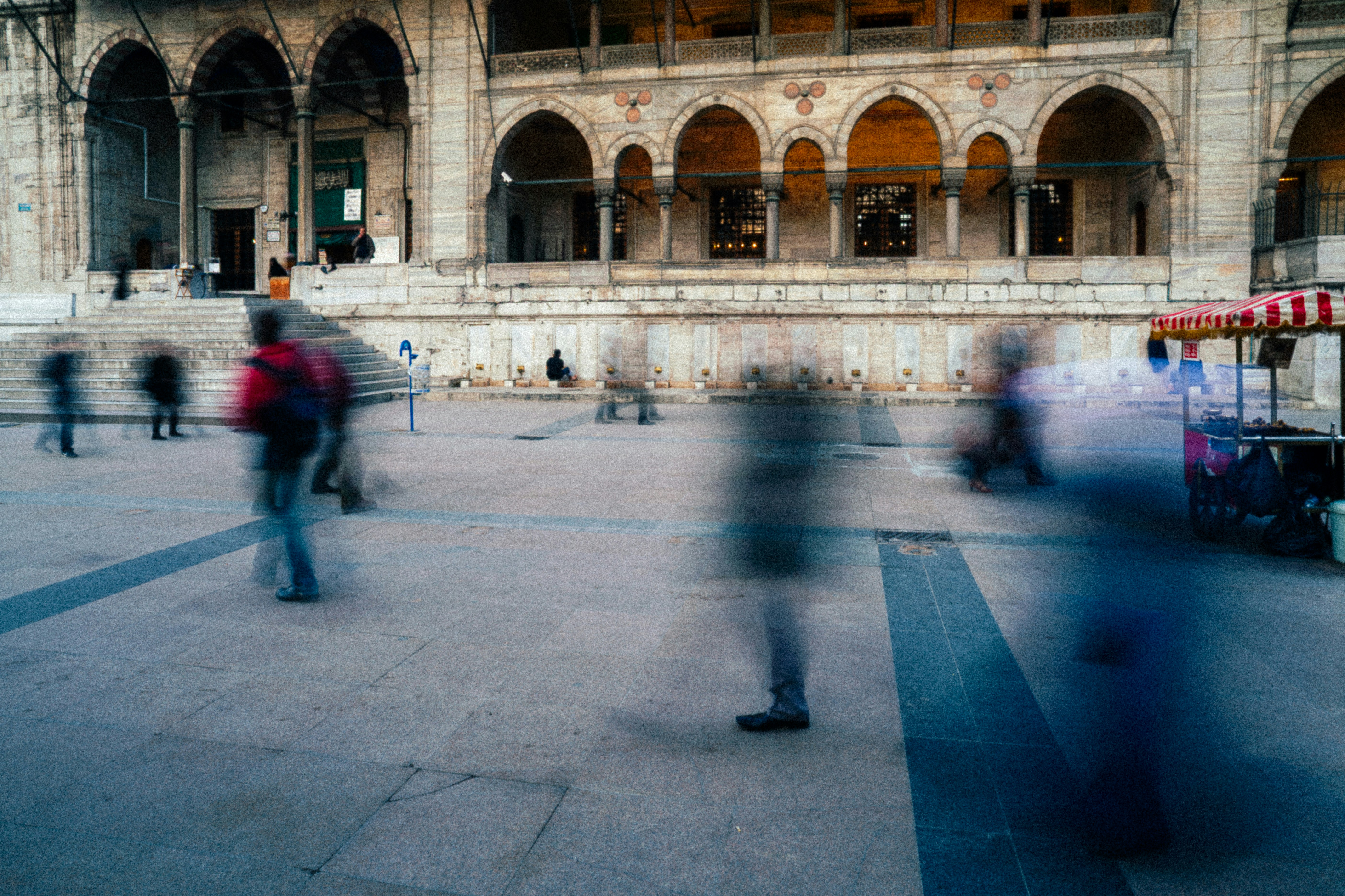 blurry figures of people walking in a plaza