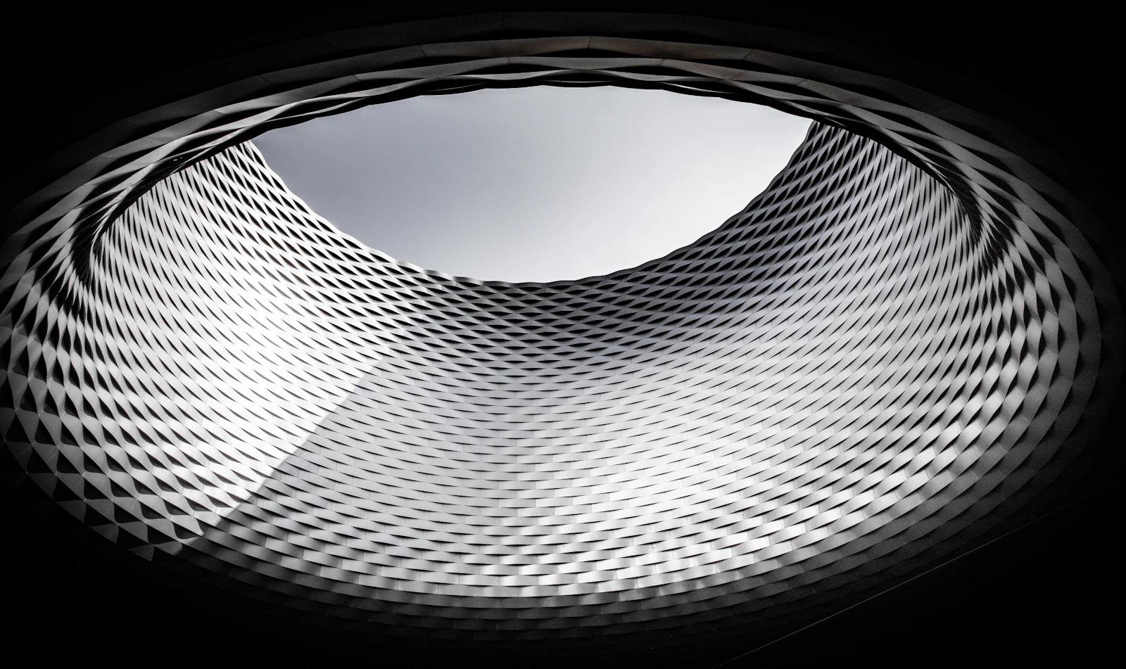 Abstract metallic tunnel of repeating ribbed lines converging toward a bright light at the far end