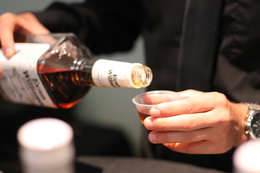 Pouring amber liquid from bottle into small cup