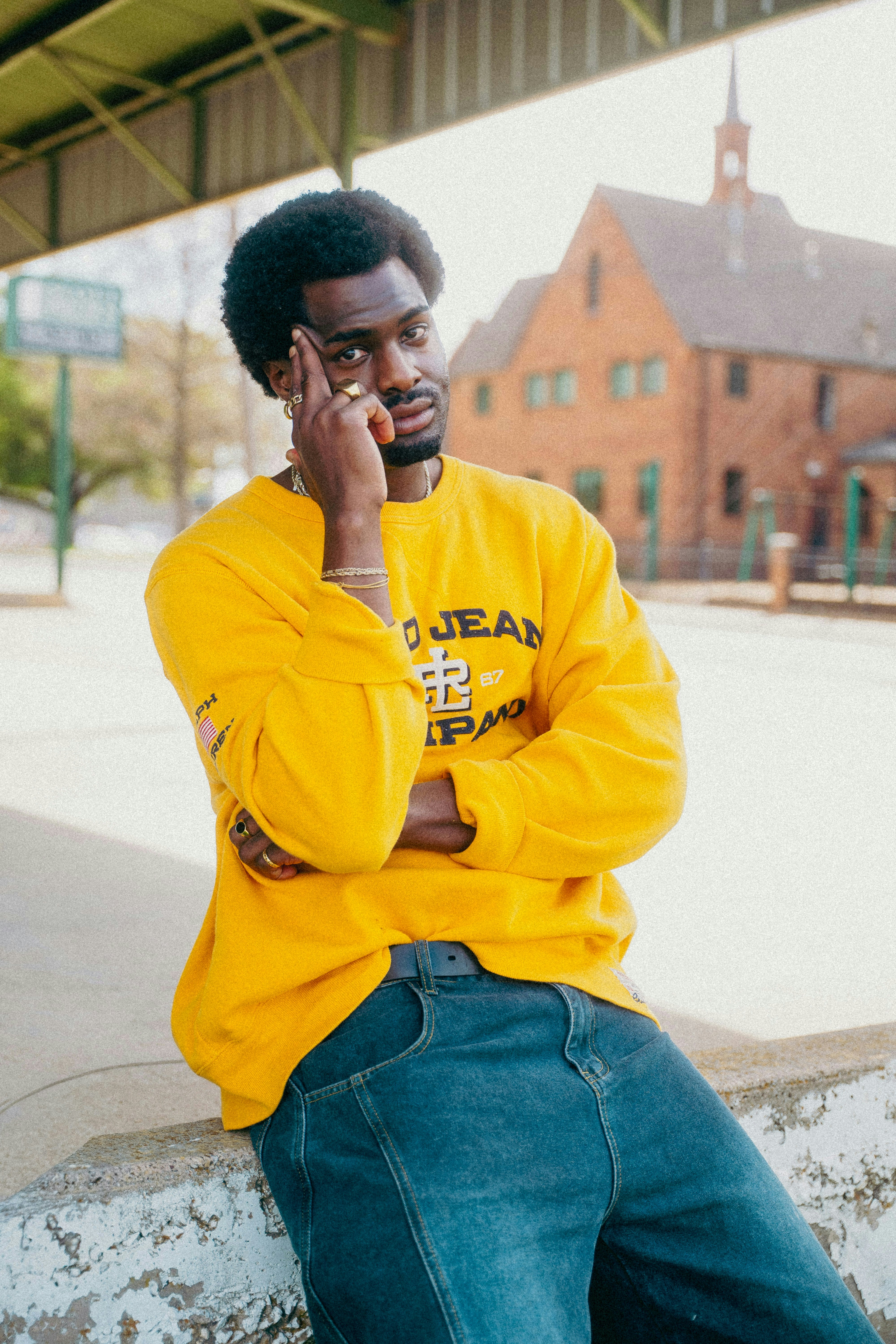 Man in yellow sweatshirt and jeans posing outdoors