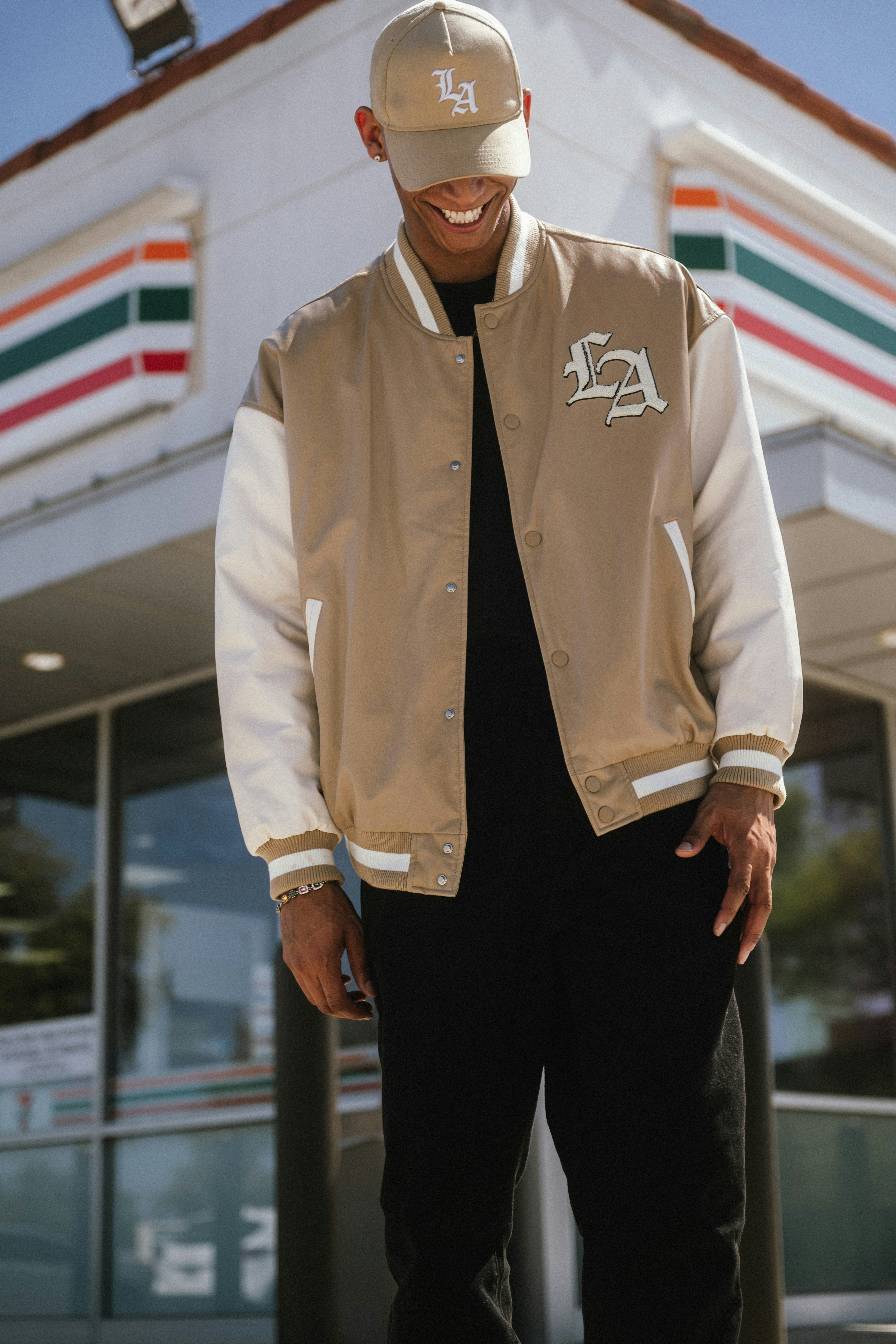 Man in a letterman jacket and baseball cap smiles.