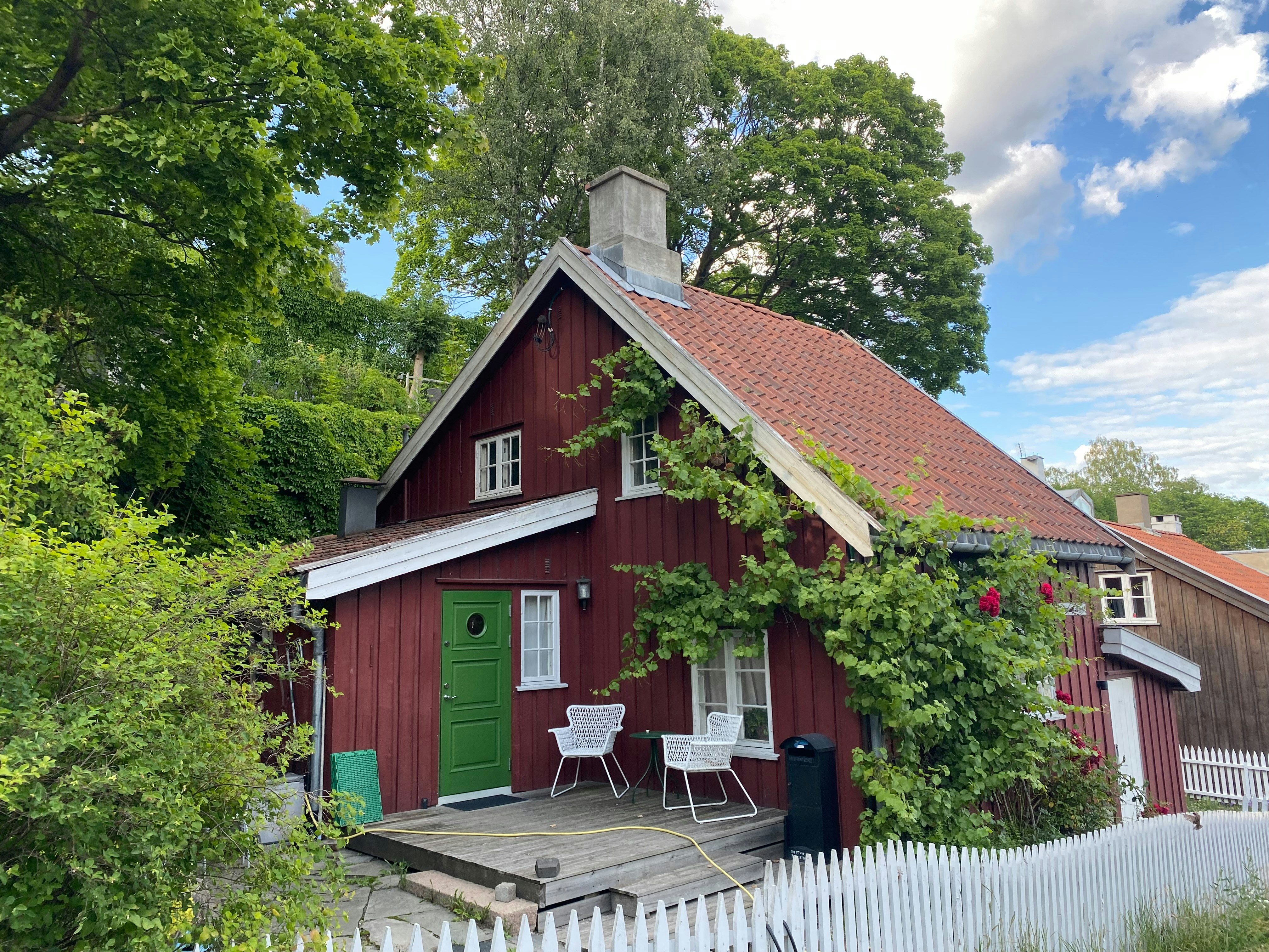 Rotes Holzhaus mit grüner Tür und weißen Stühlen.