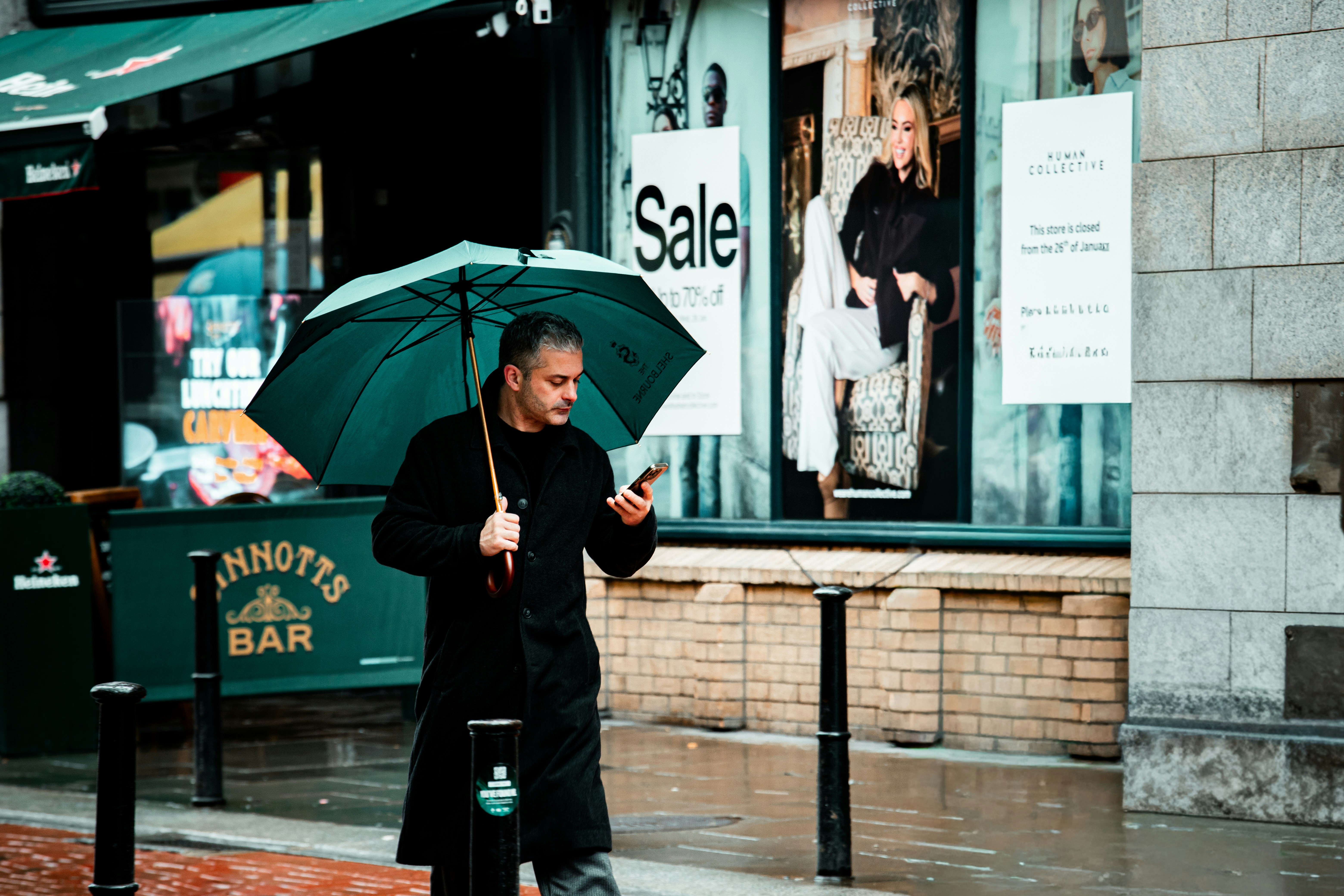 Man with umbrella checks phone on rainy street
