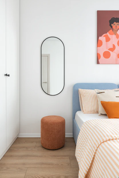 A minimalist bedroom with a blue bed and orange stool.