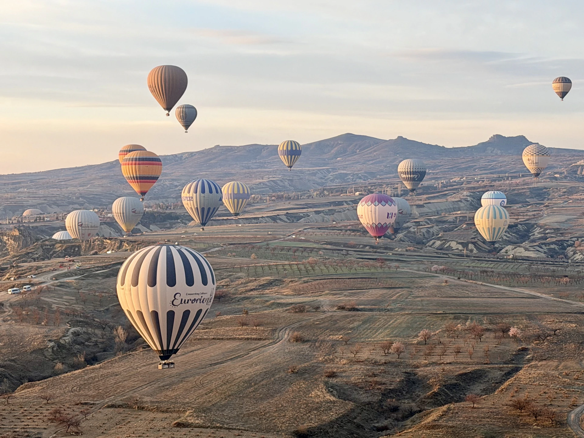 Hot air balloons float over a mountainous landscape at sunrise.