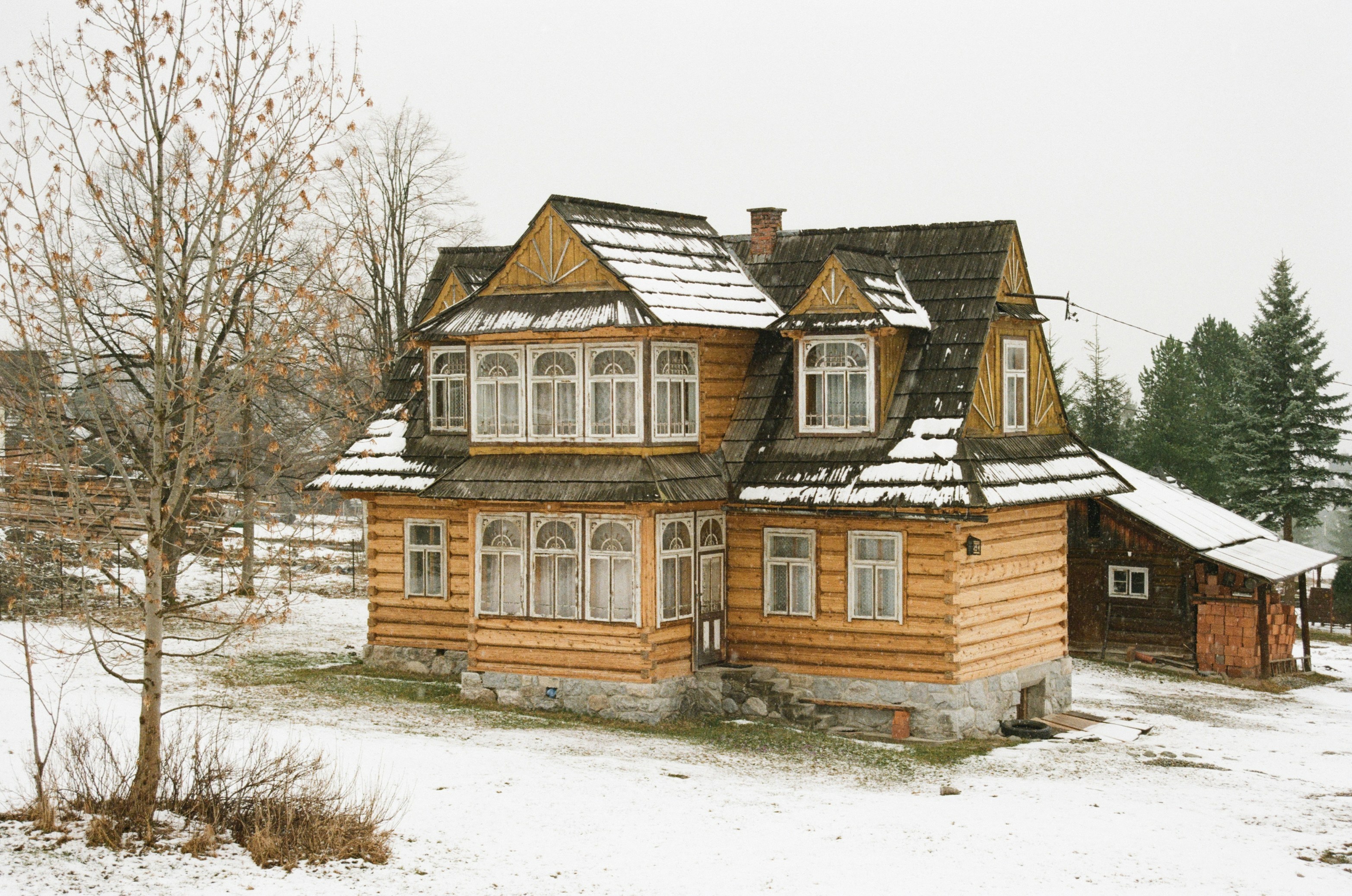 Wooden house with snow on the roof and trees.