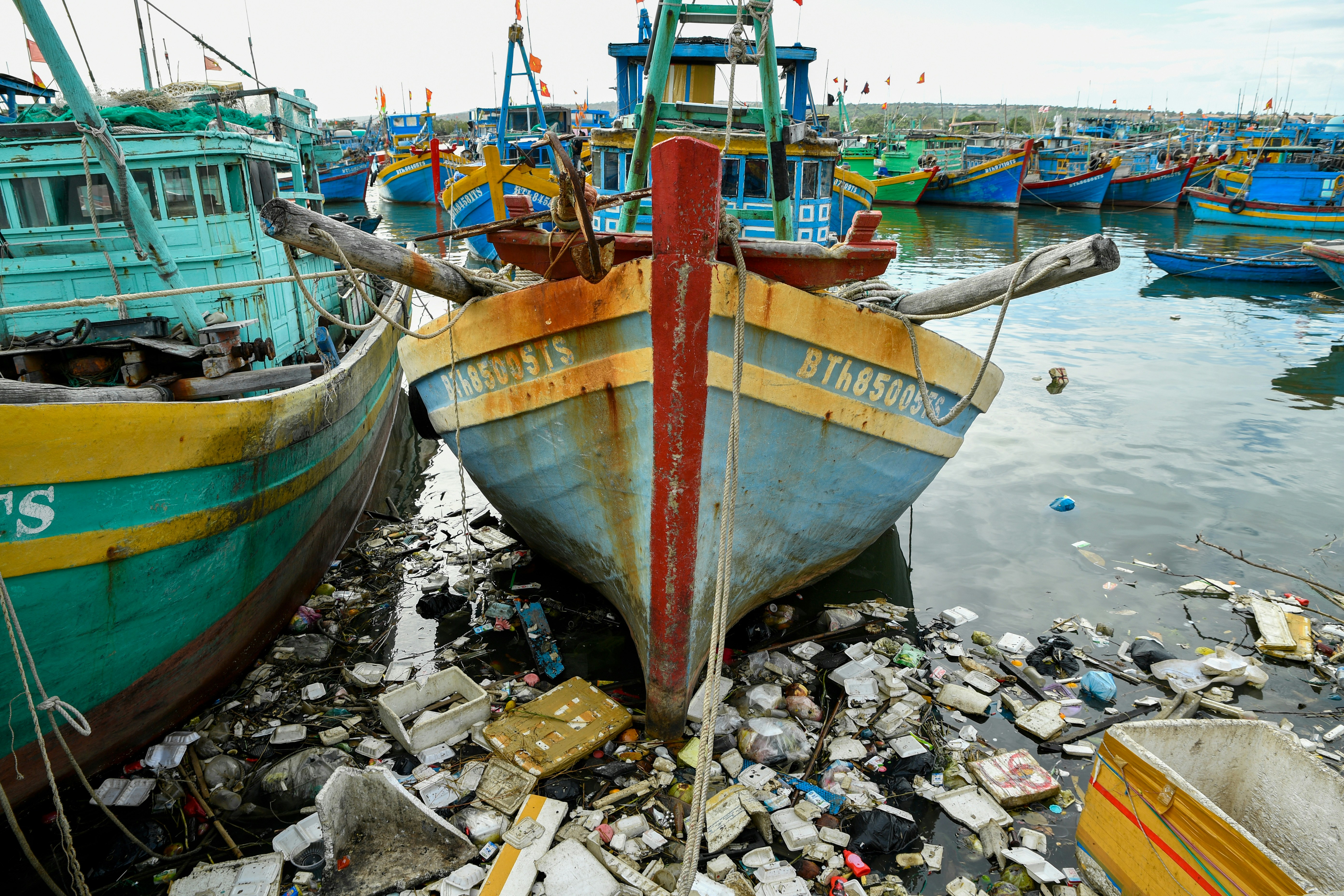 Fishing boats docked in a harbor filled with trash.