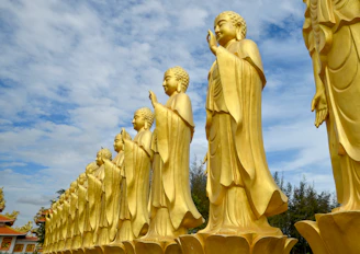 Row of golden buddha statues against a cloudy sky