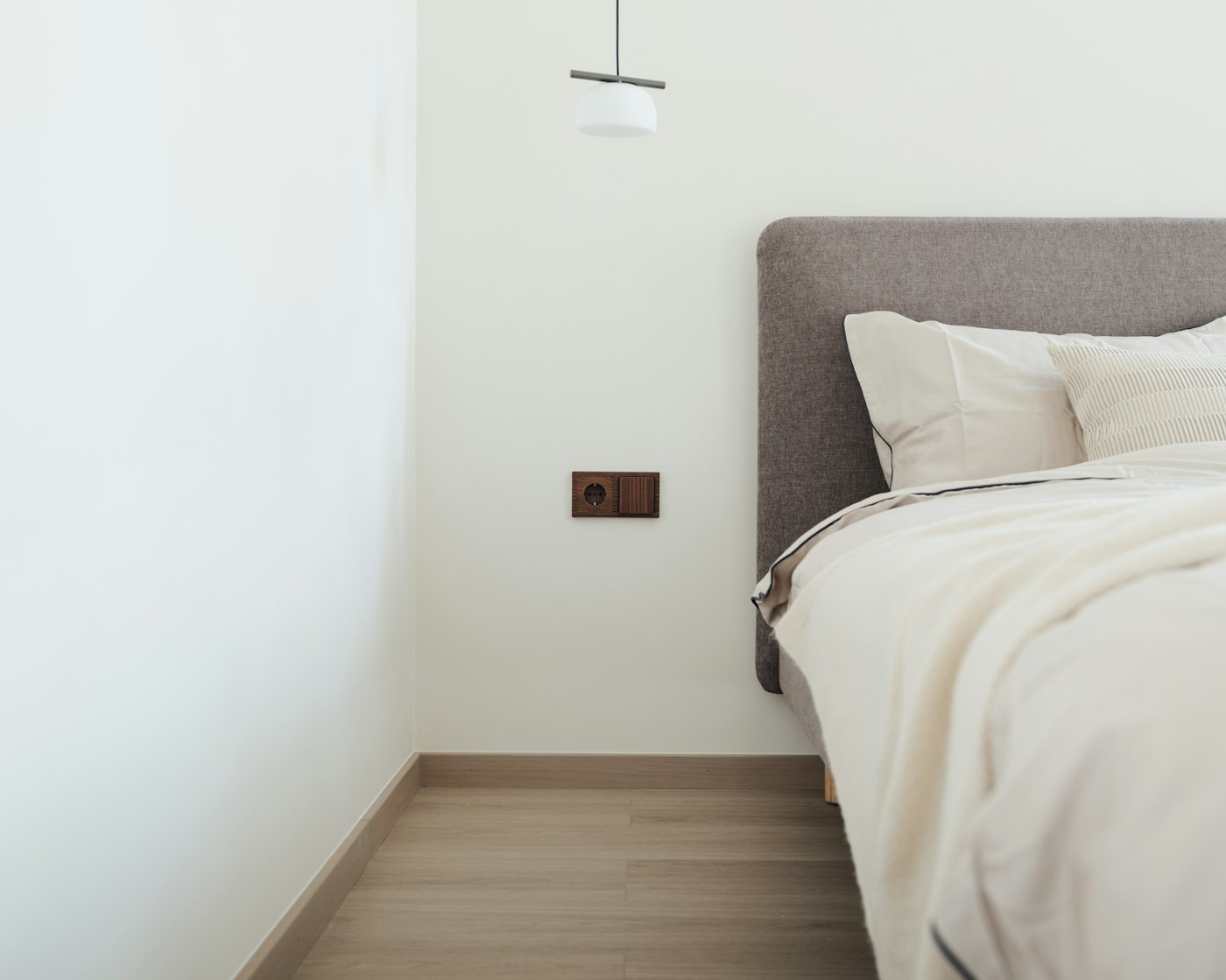 Japandi minimalist bedroom with cream linen bedding, gray upholstered headboard, oak floor, and a single small pendant light