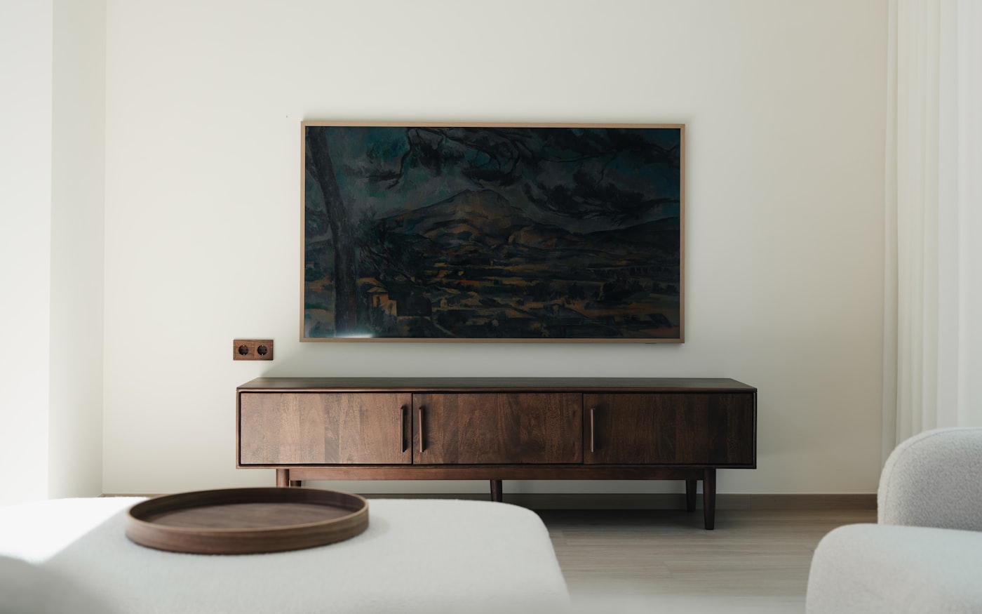 Japandi small apartment with dark walnut credenza, soft cream boucle armchair, walnut tray on white ottoman, and a single muted landscape art piece