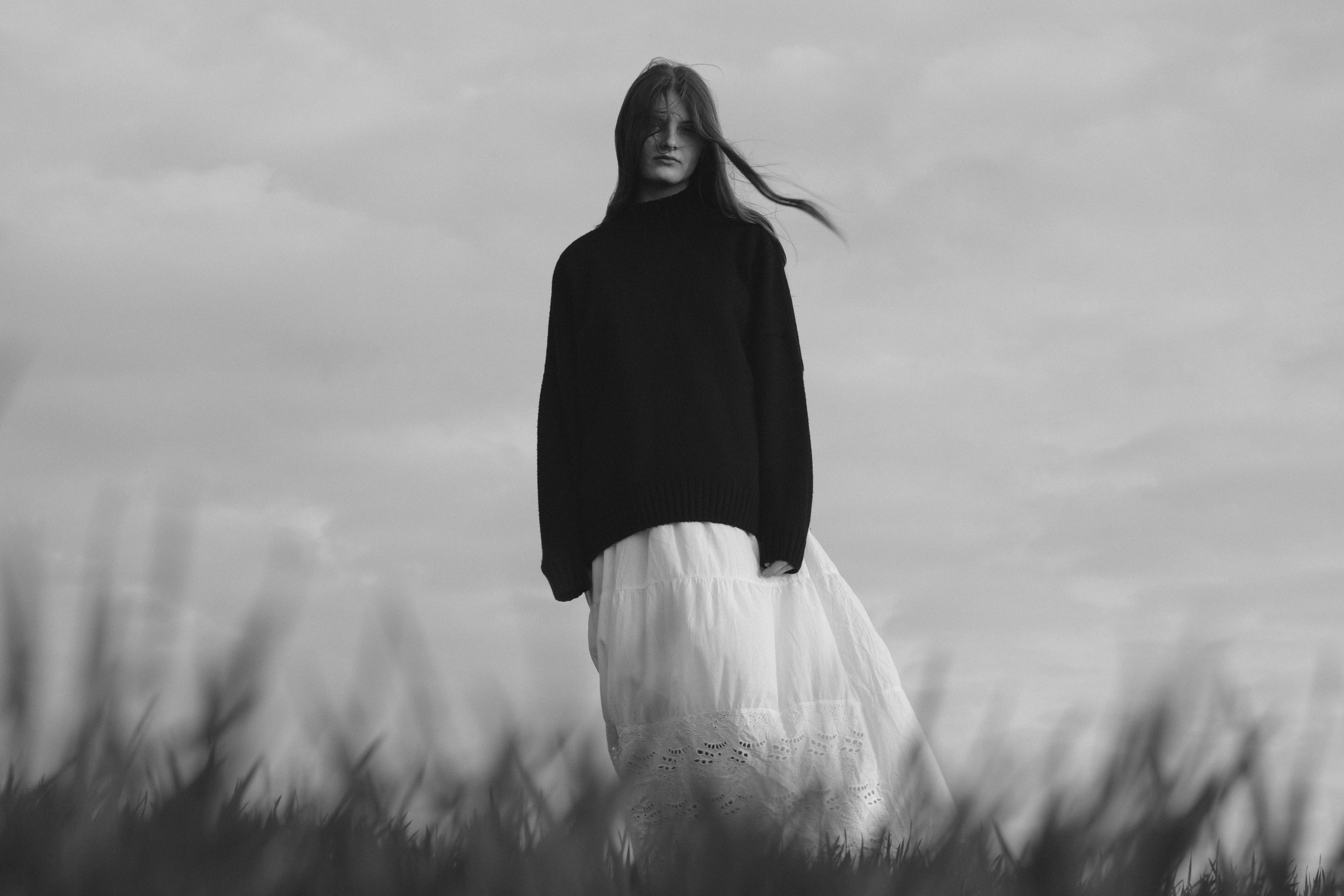 Woman in a sweater and skirt standing in a field.