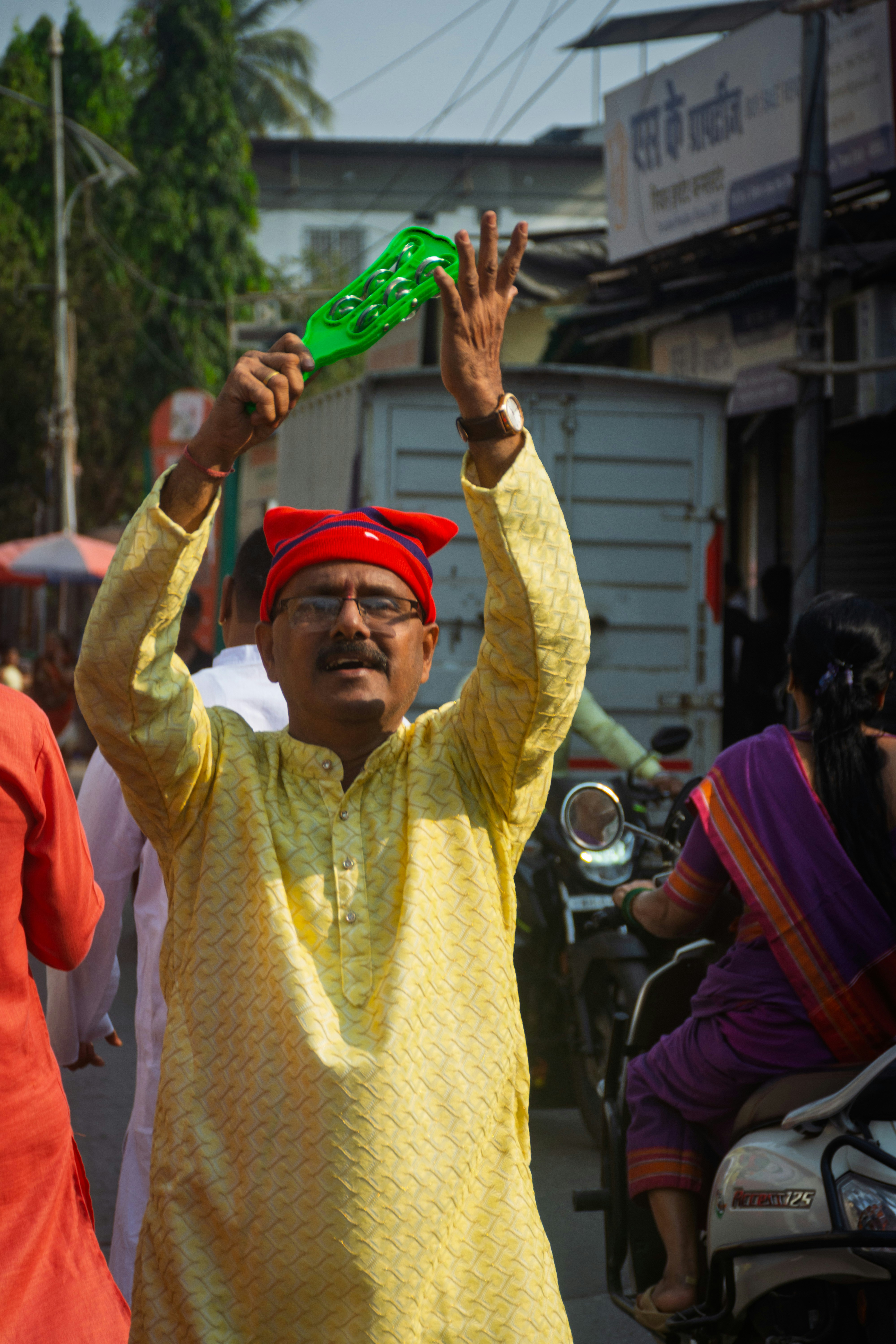 Man in yellow kurta waves green fan at street event