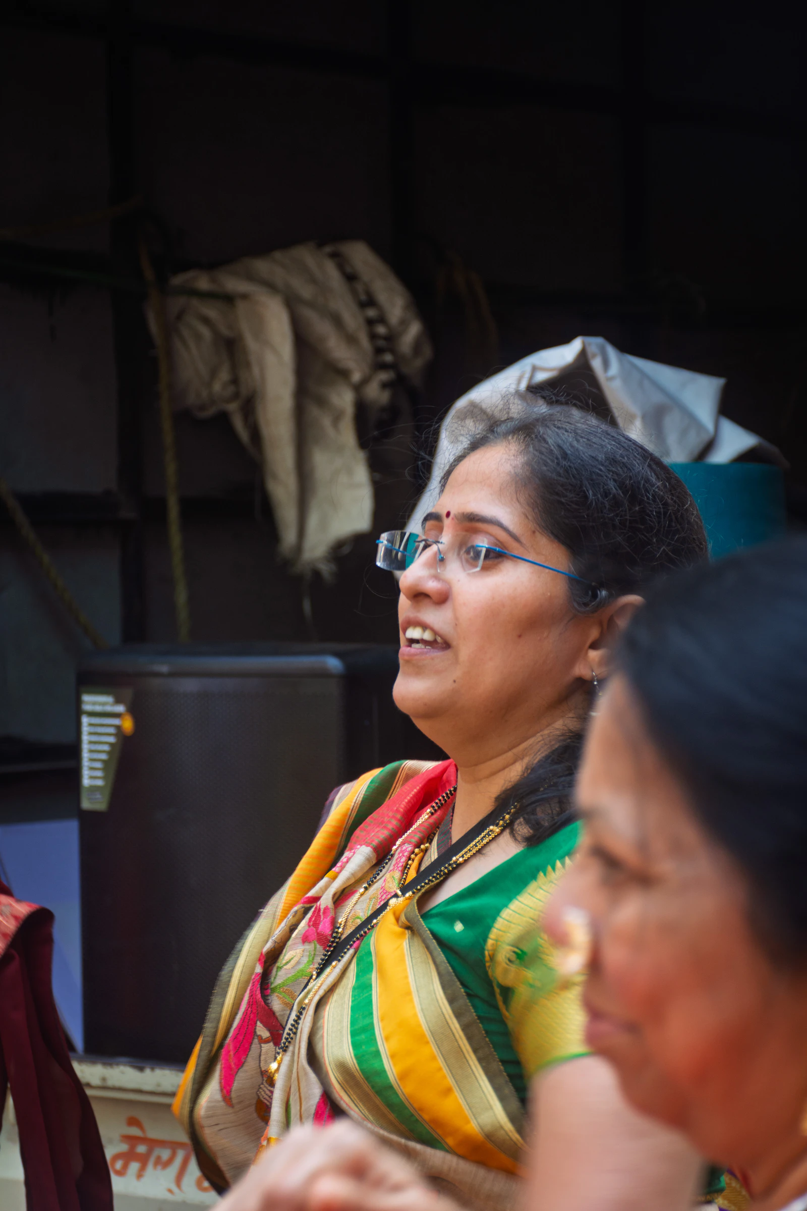A woman wearing glasses and a colourful sari, mid-conversation