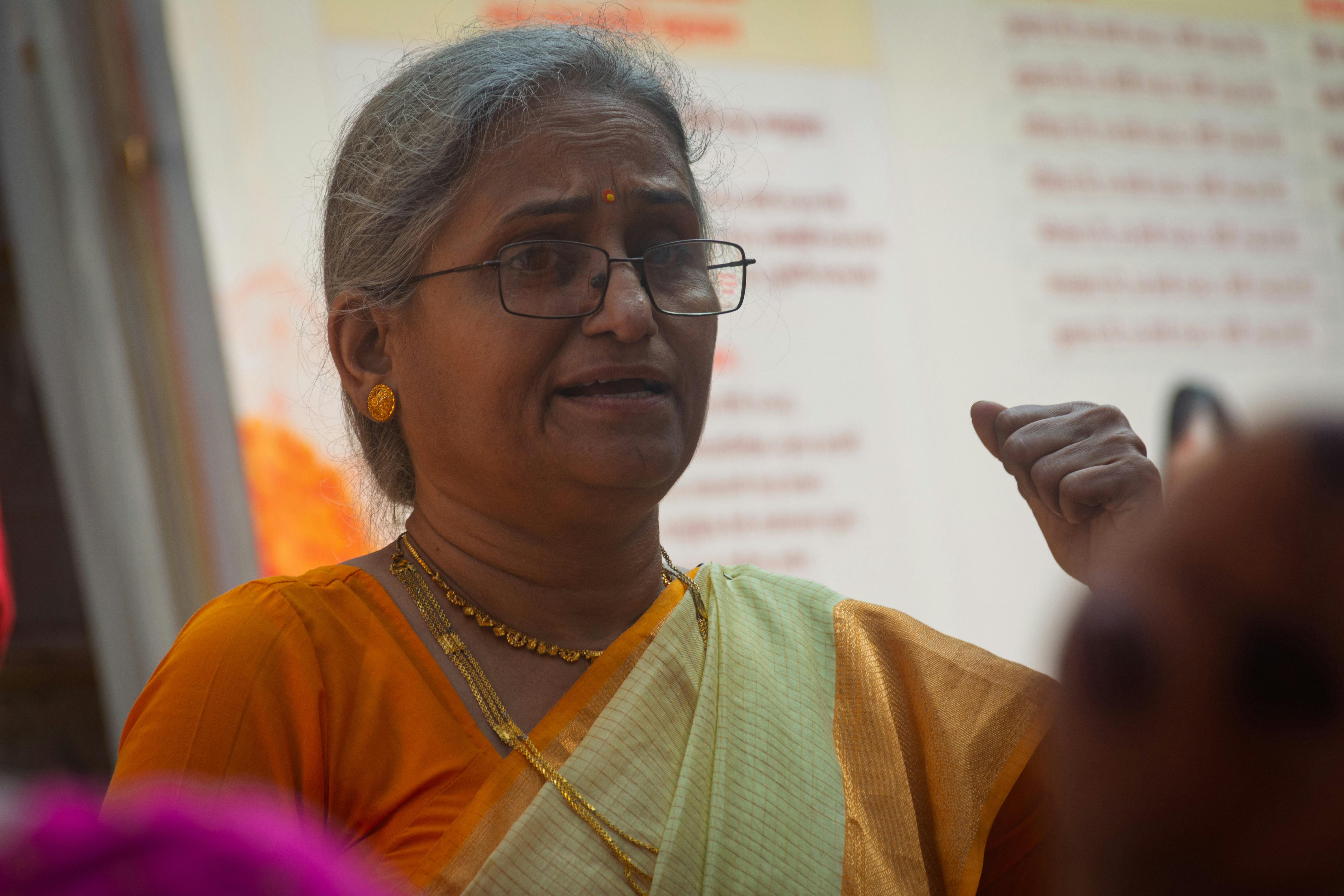 Une vieille femme indienne portant des lunettes et un sari parle.