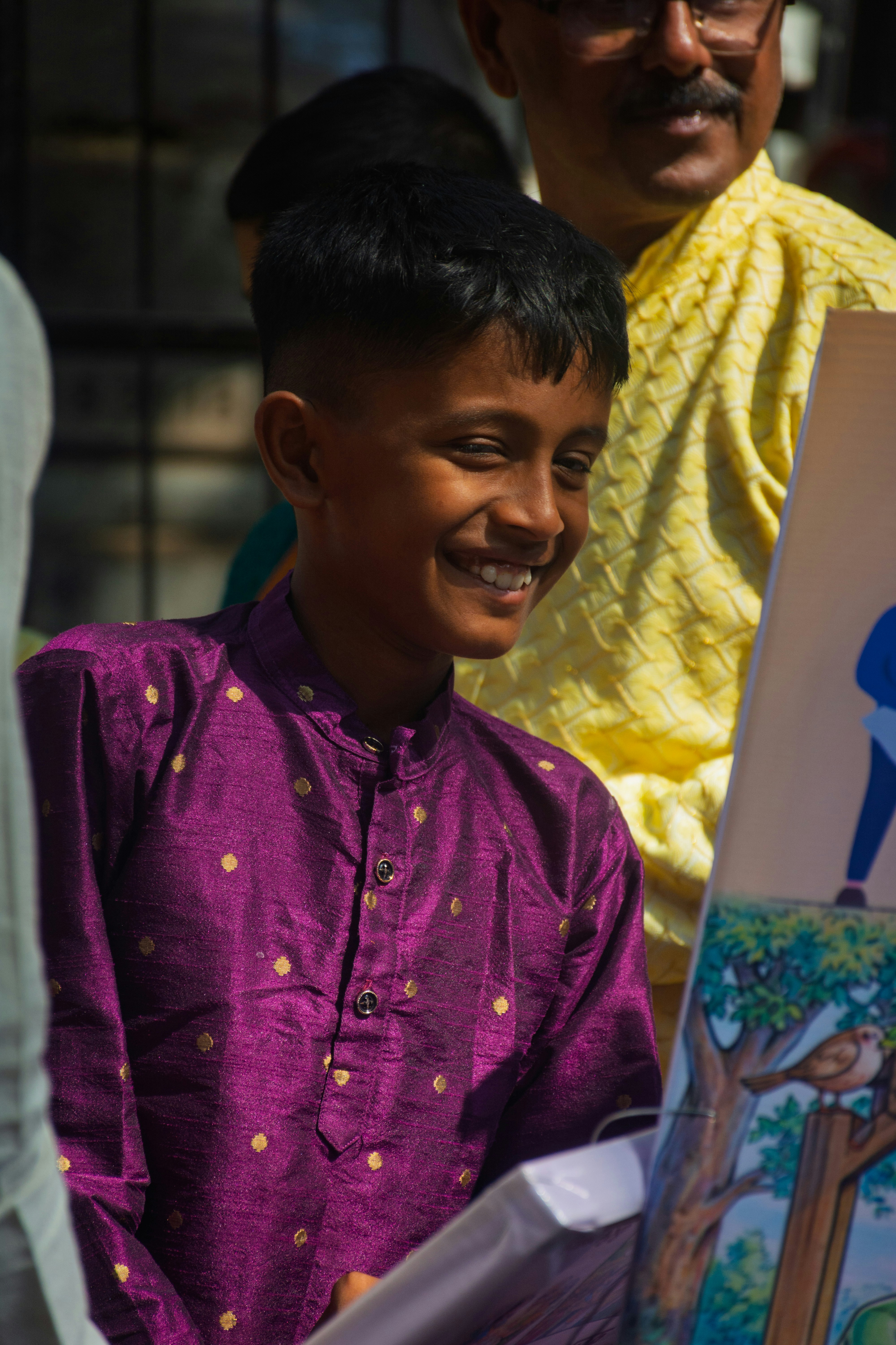 A young boy in a purple kurta smiles brightly smiles.