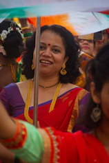 A smiling woman in a red sari with gold jewelry.