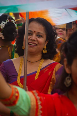A smiling woman in a red sari with gold jewelry.