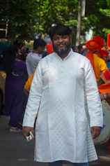 Man in white kurta with beard smiles holding phone