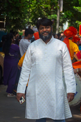 Man in white kurta with beard smiles holding phone