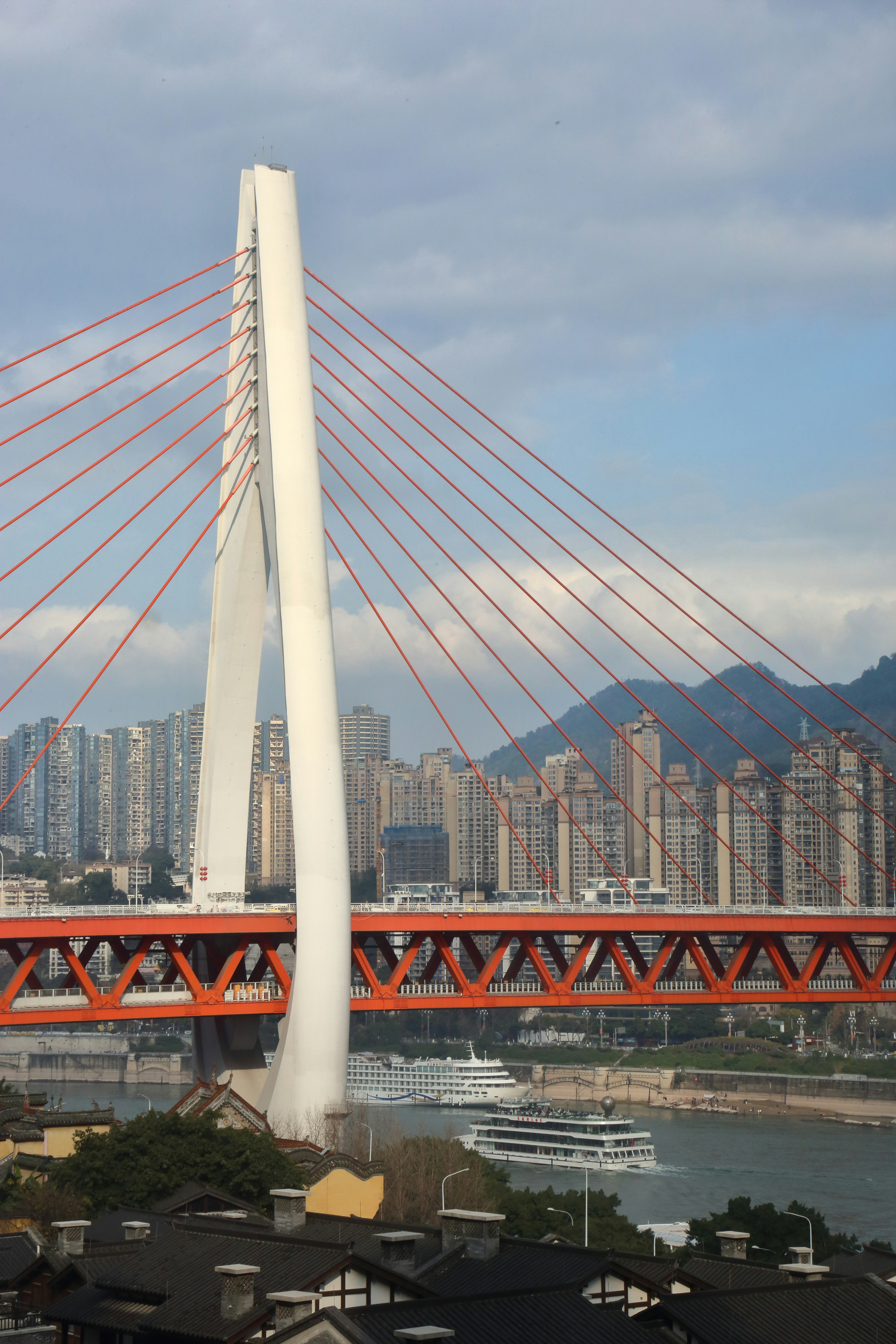 Uma ponte moderna estaiada atravessa um rio com o horizonte da cidade.