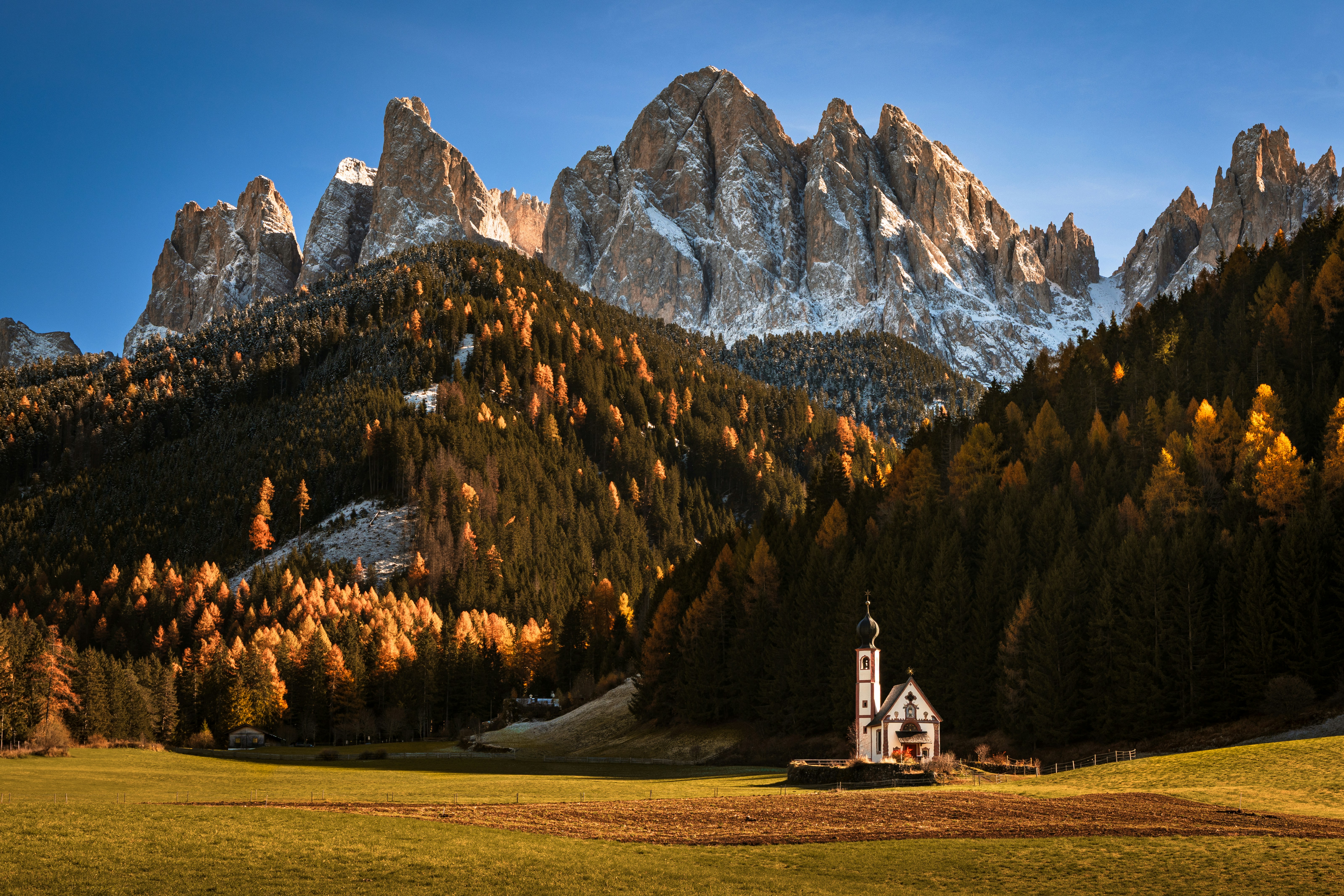 Small church in a valley with autumn trees and mountains.