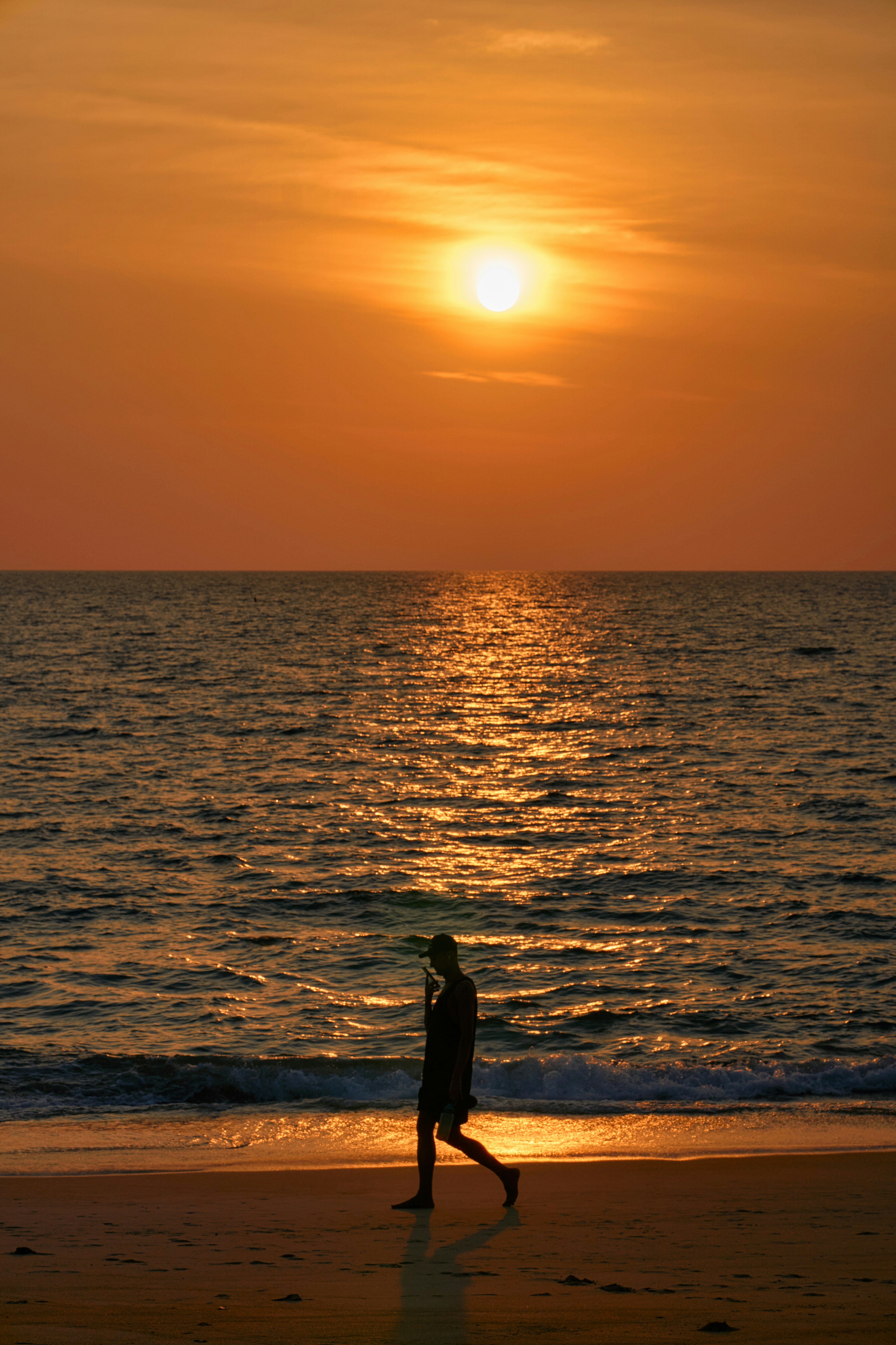 Silhouette einer Person, die bei Sonnenuntergang am Strand entlanggeht.