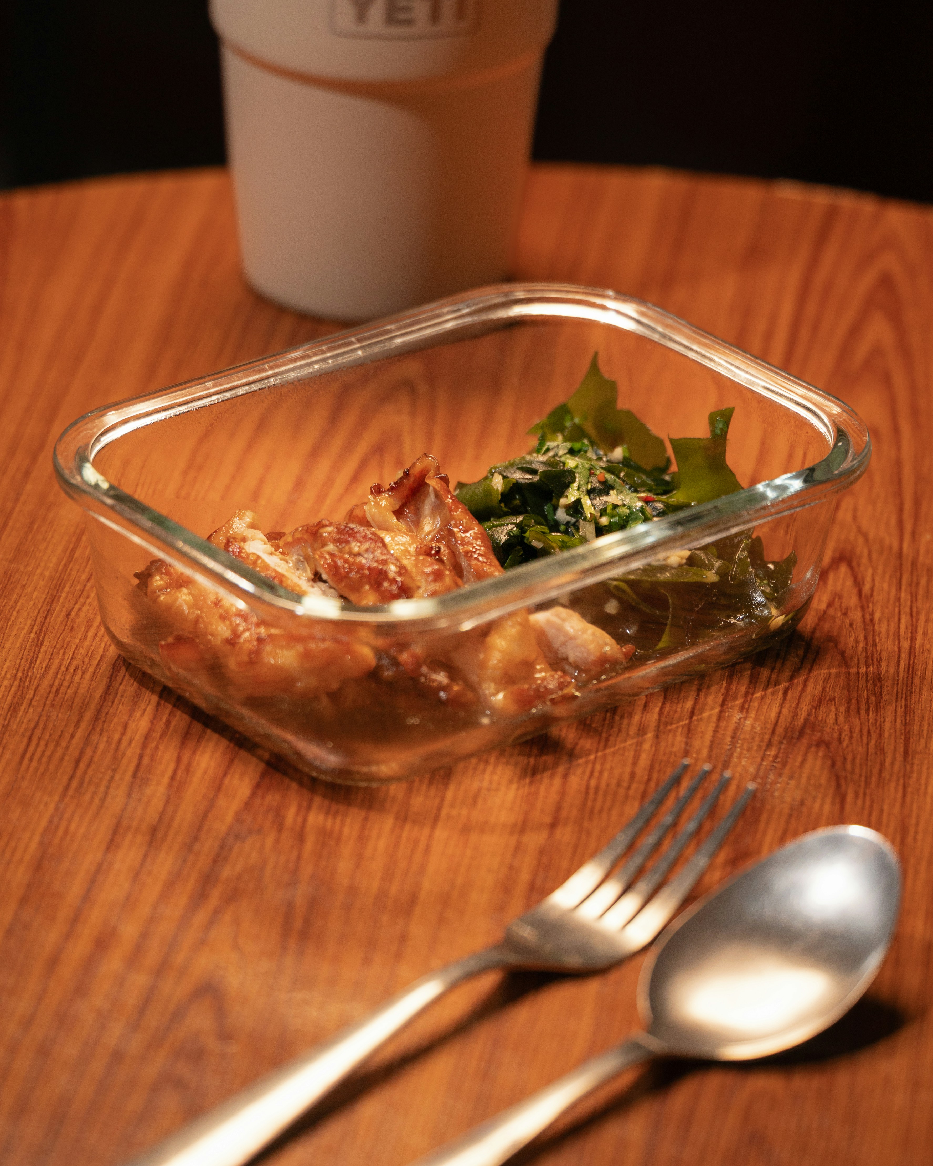 Huhn und Grünzeug in einem Glasbehälter mit Besteck.