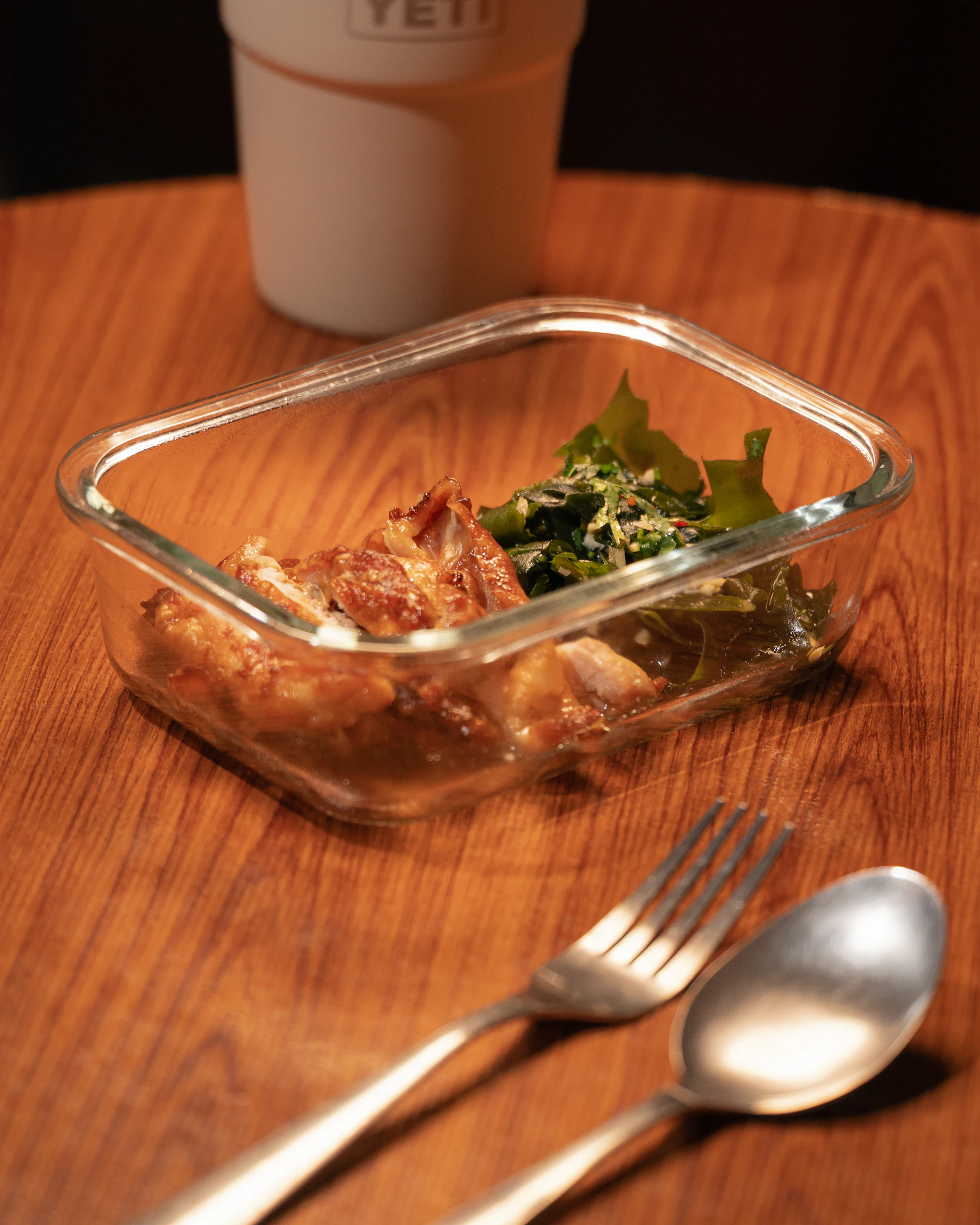 Leftovers in a shallow glass container on a wooden table with a fork and spoon beside it