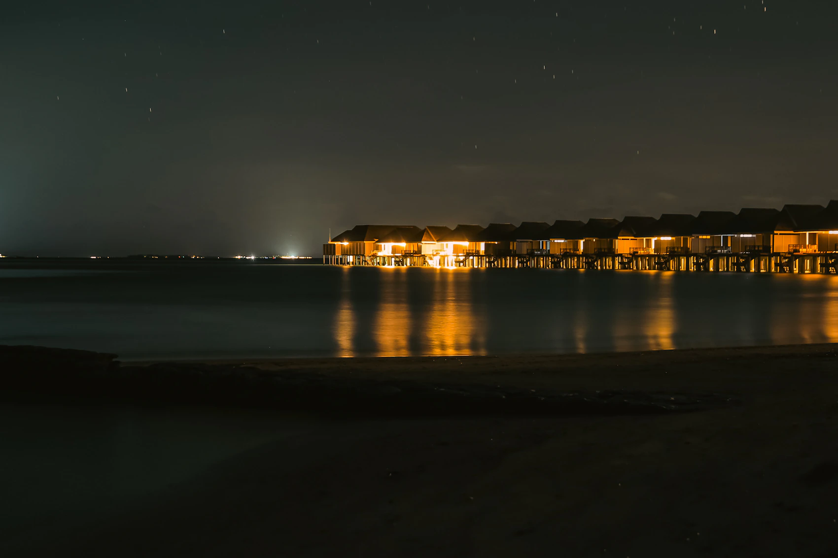 Overwater villas illuminated at night above calm water in the Maldives