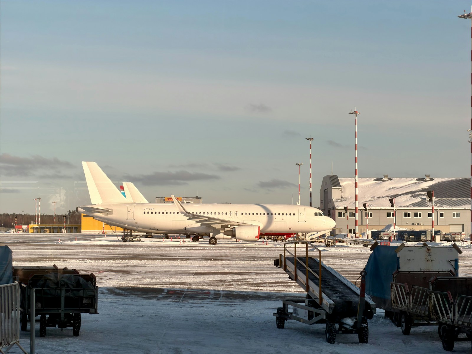 A white passenger jet parked on a snowy airport apron beside baggage carts and an operations building