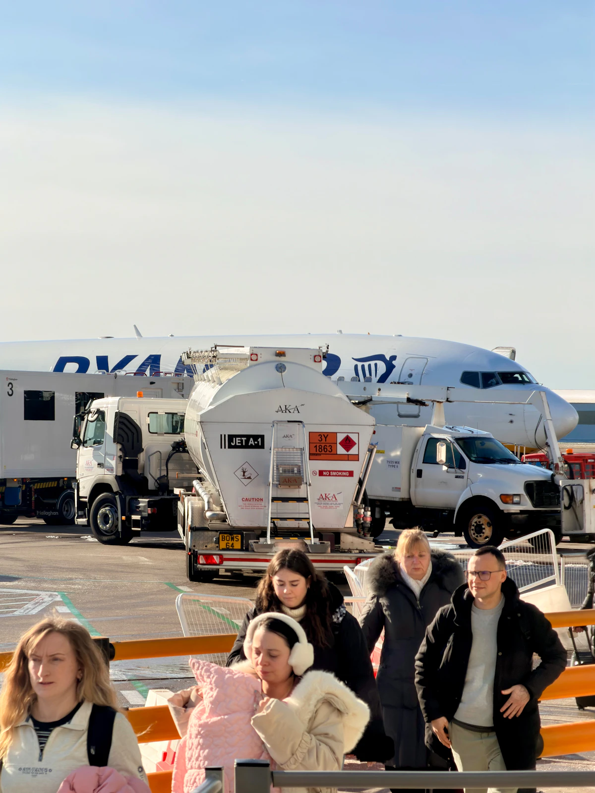 People walk past an airplane being refueled at an airport