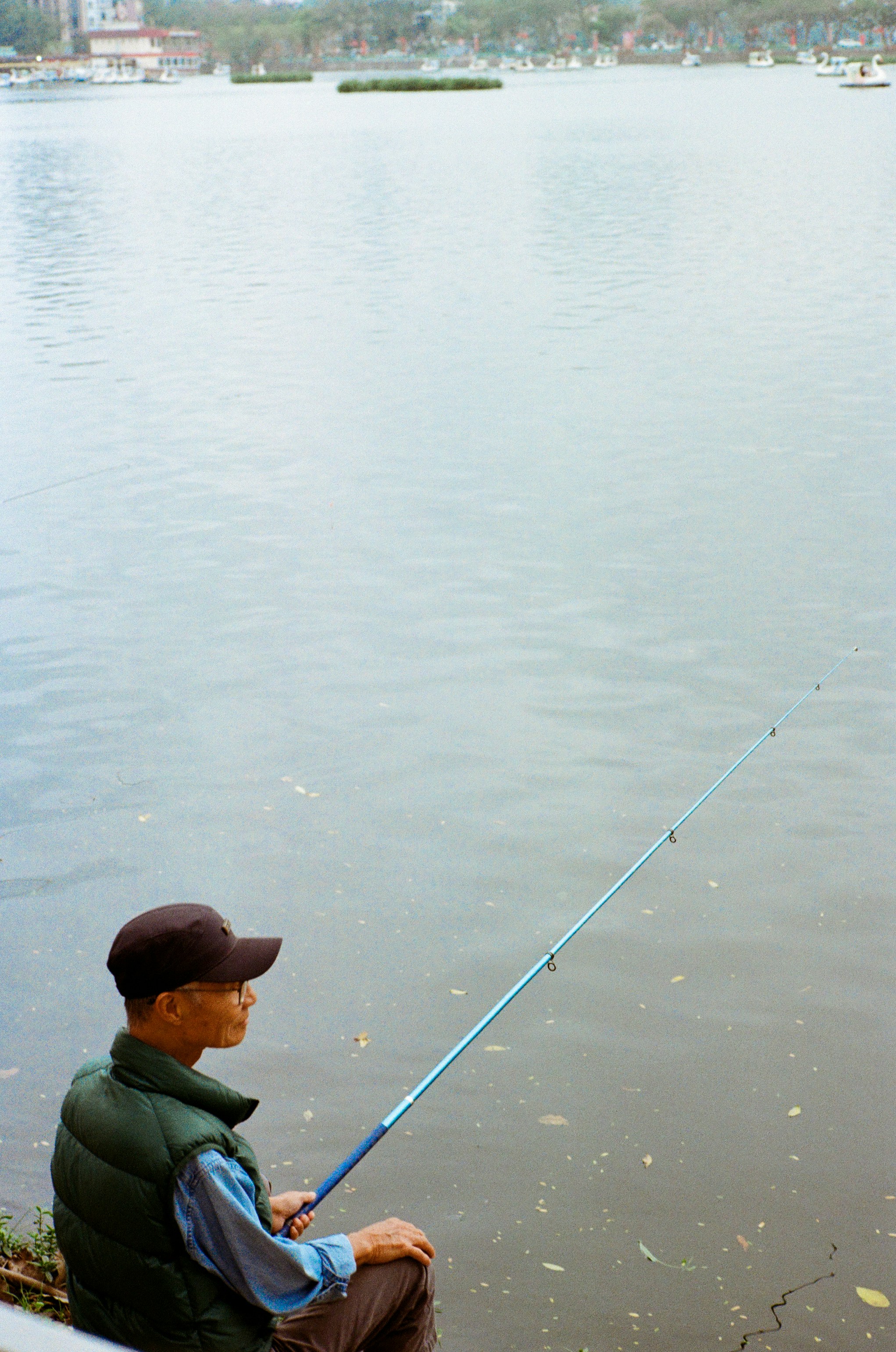 Man fishing by a calm lake with buildings in distance