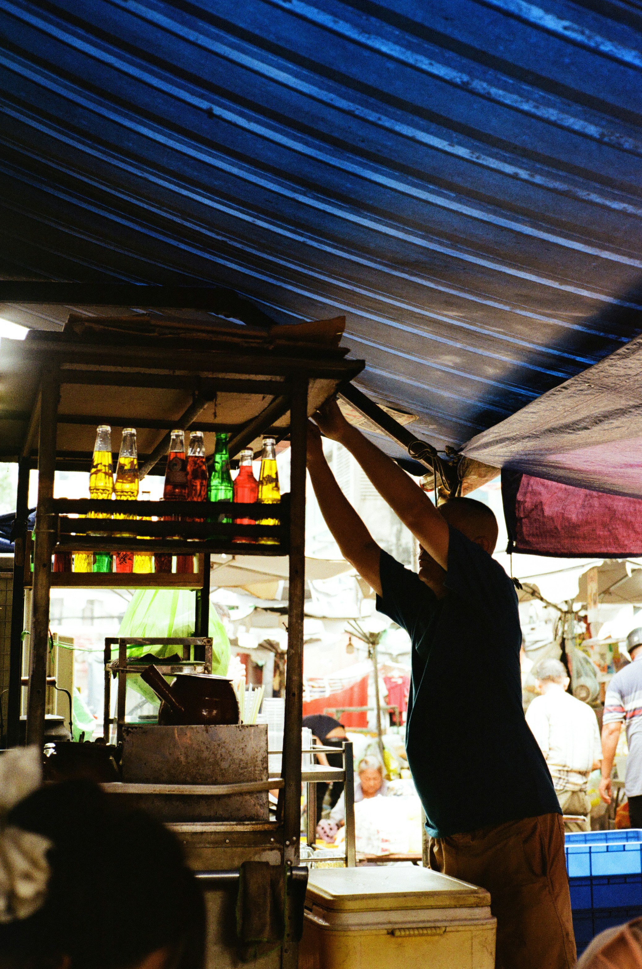 Man reaching for colorful bottles under blue awning