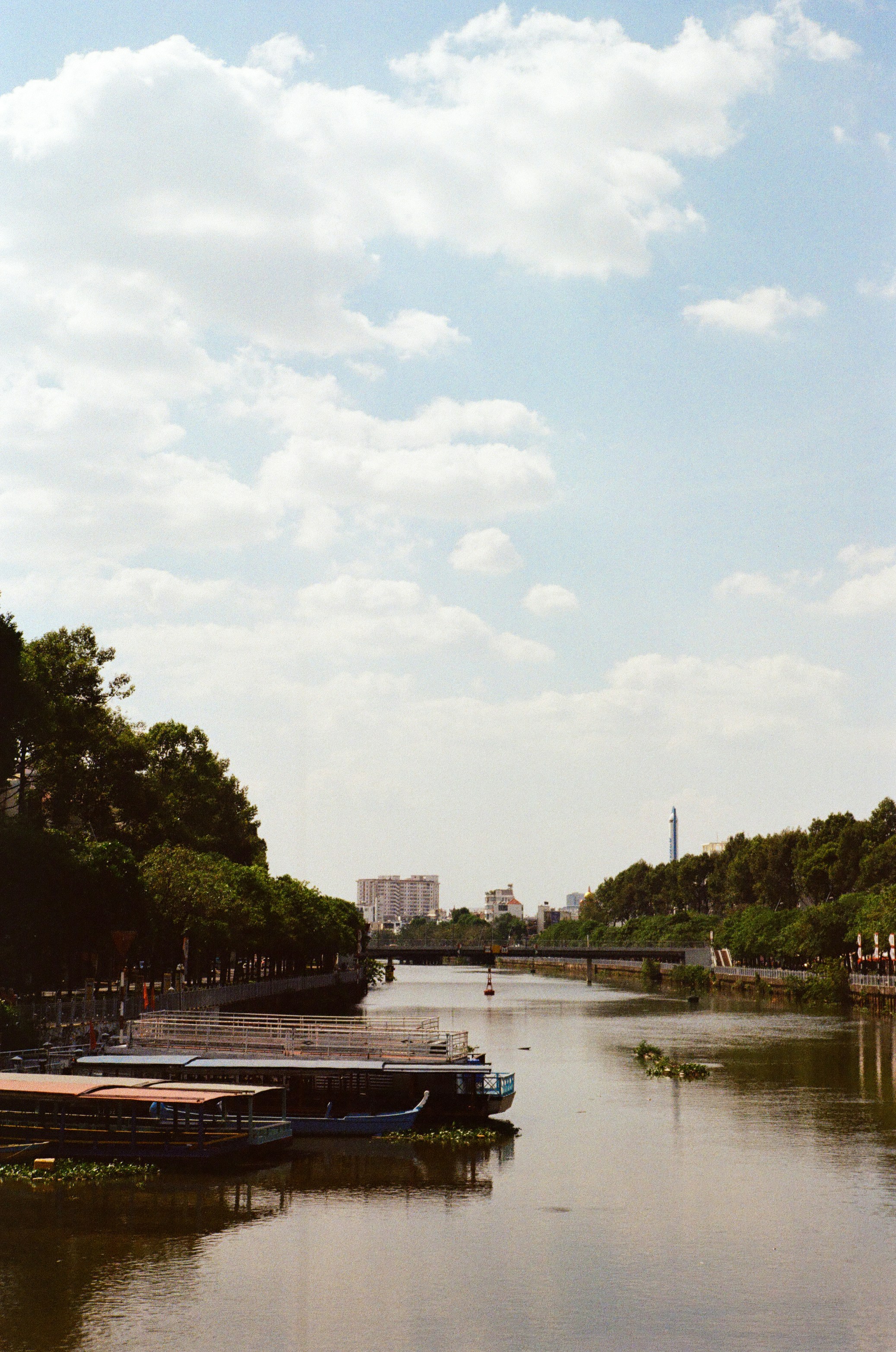 Boats docked on a river with cityscape in background.