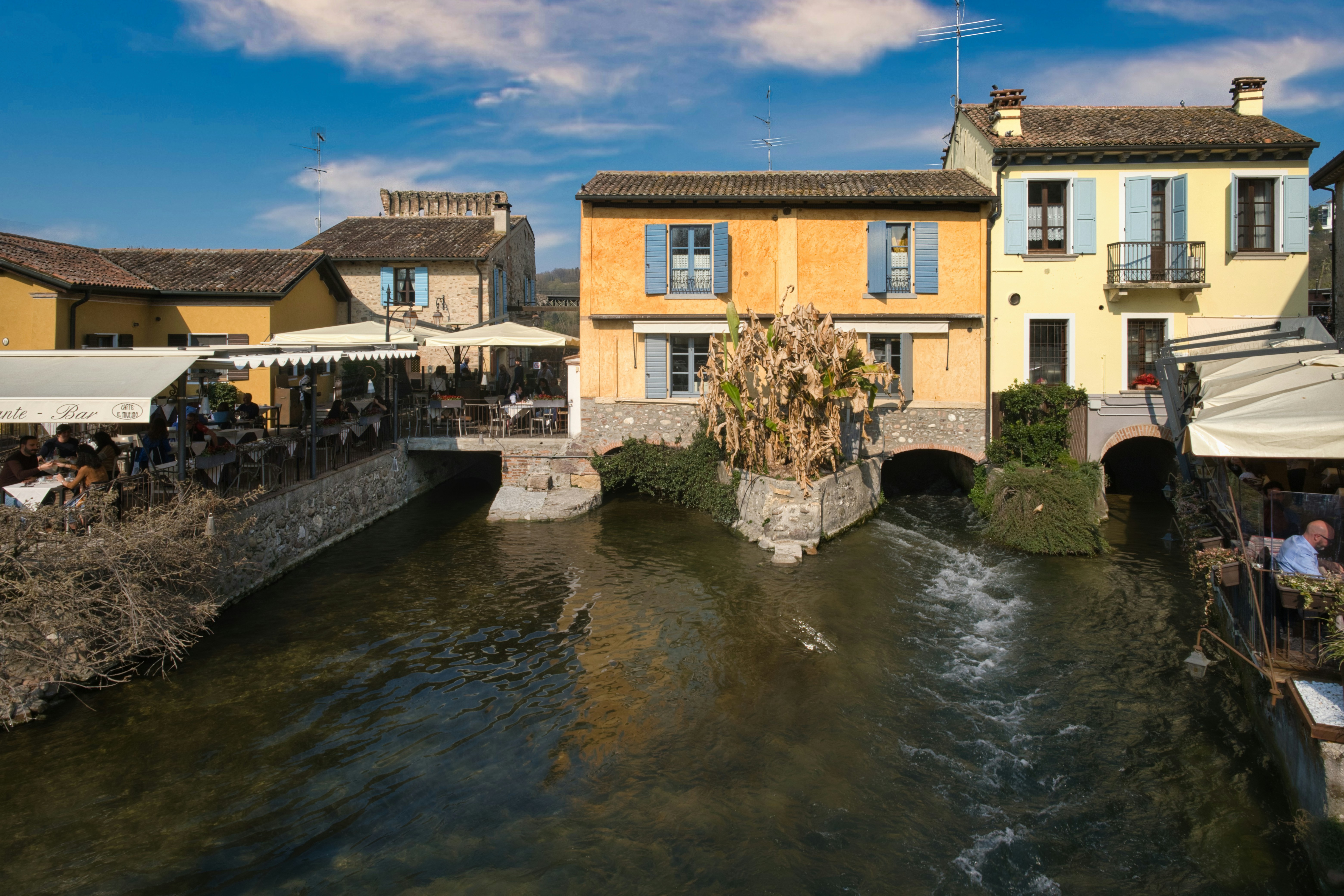 Buildings line a canal with people dining outdoors.