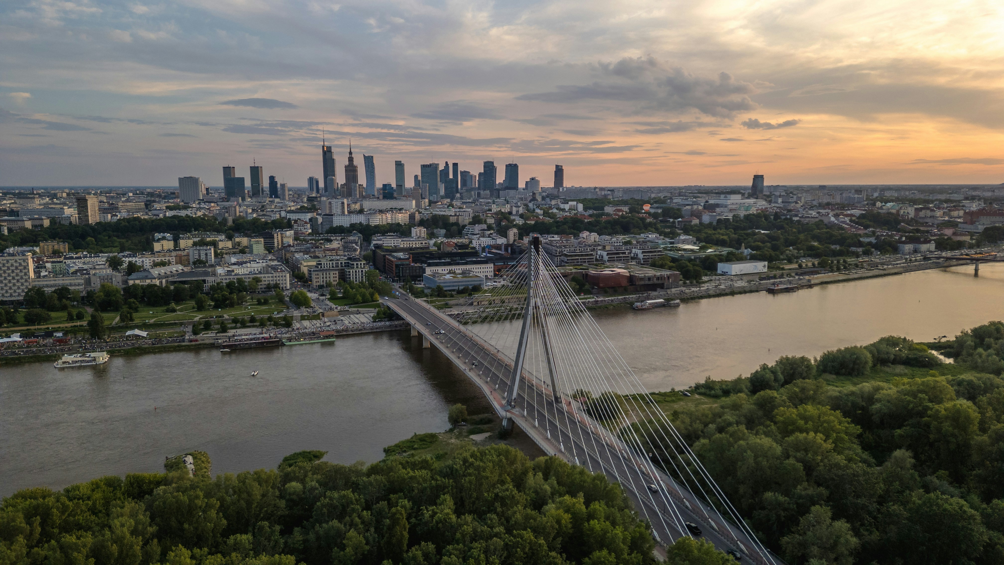 Paisaje urbano moderno con un puente sobre un río al atardecer.