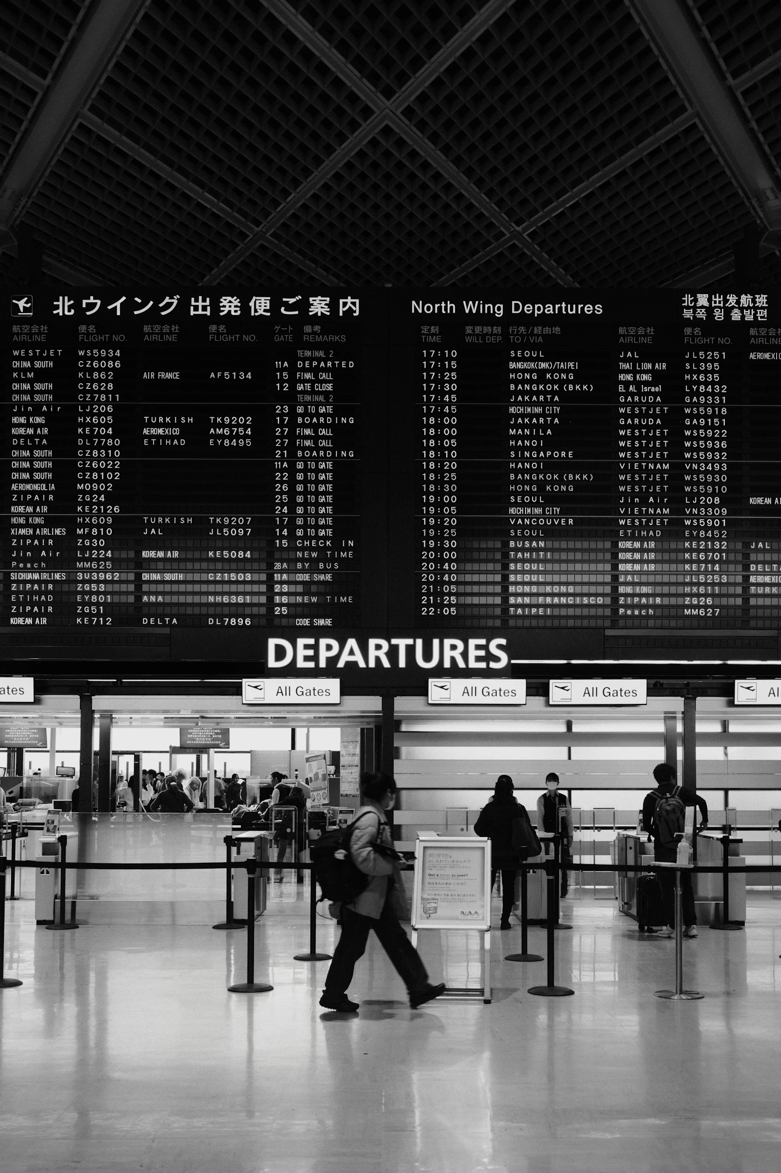 Travellers walking past an airport departure board
