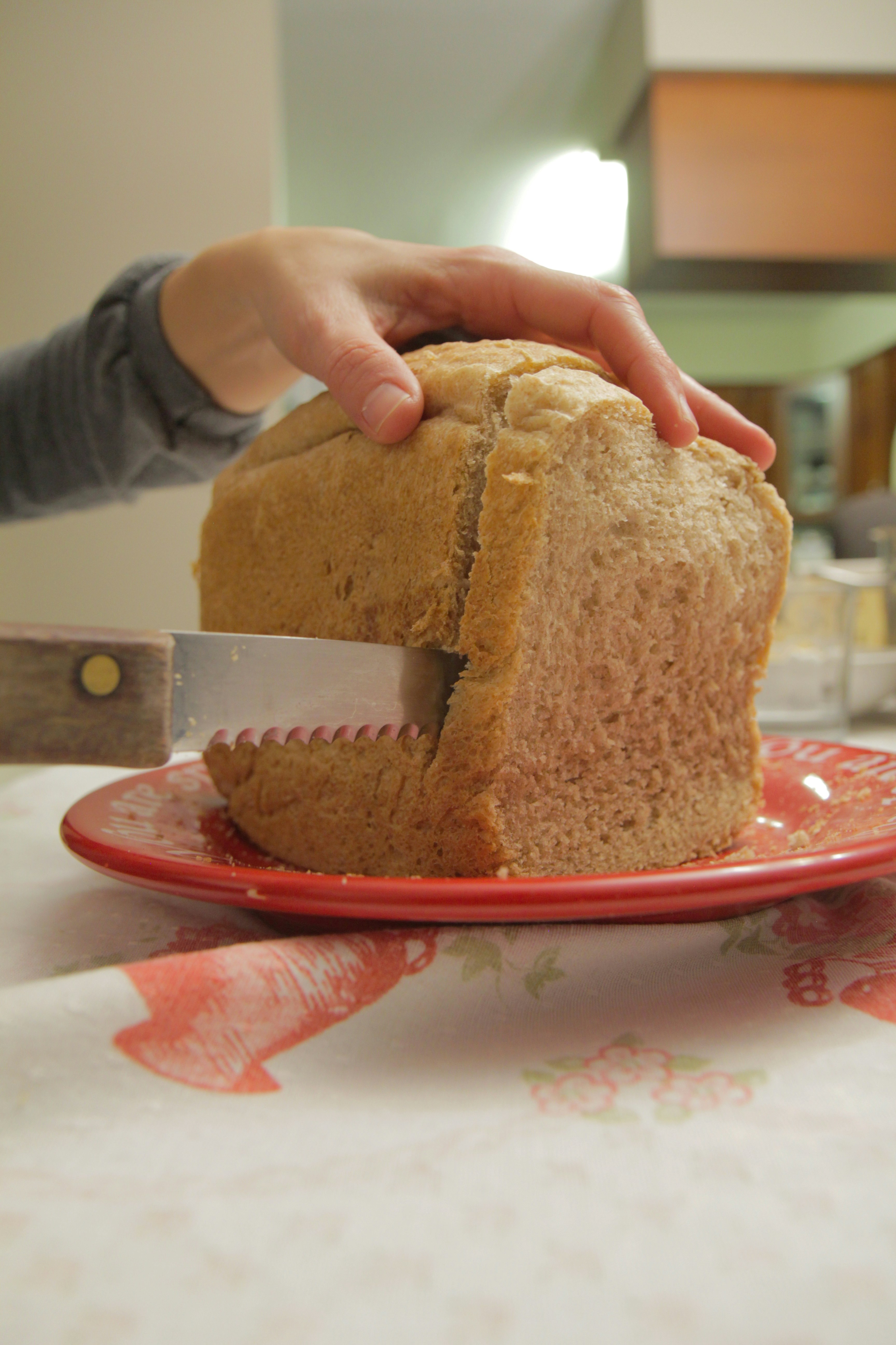 Hand slicing a loaf of bread on a red plate.
