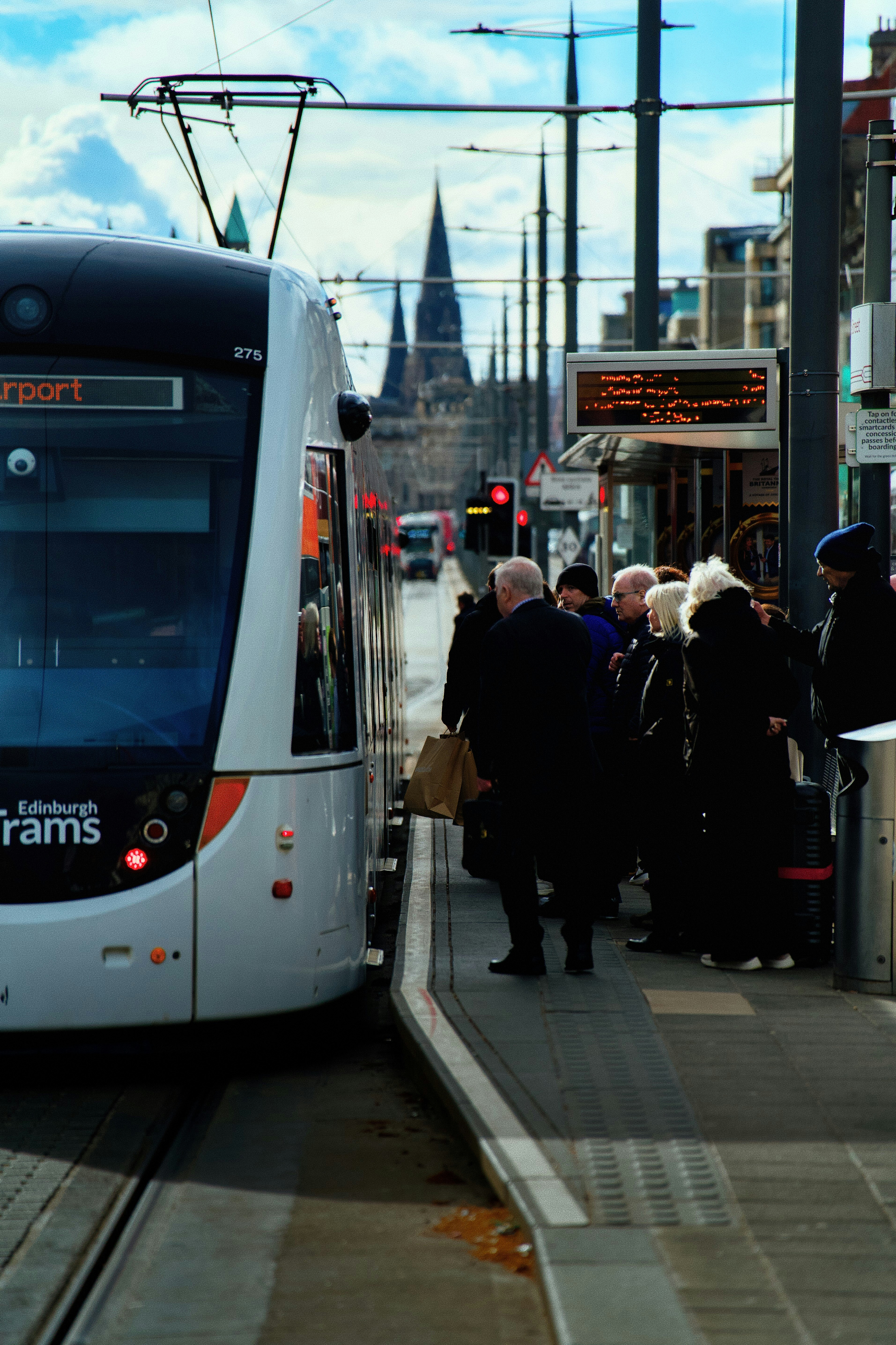People waiting for tram at station with edinburgh castle